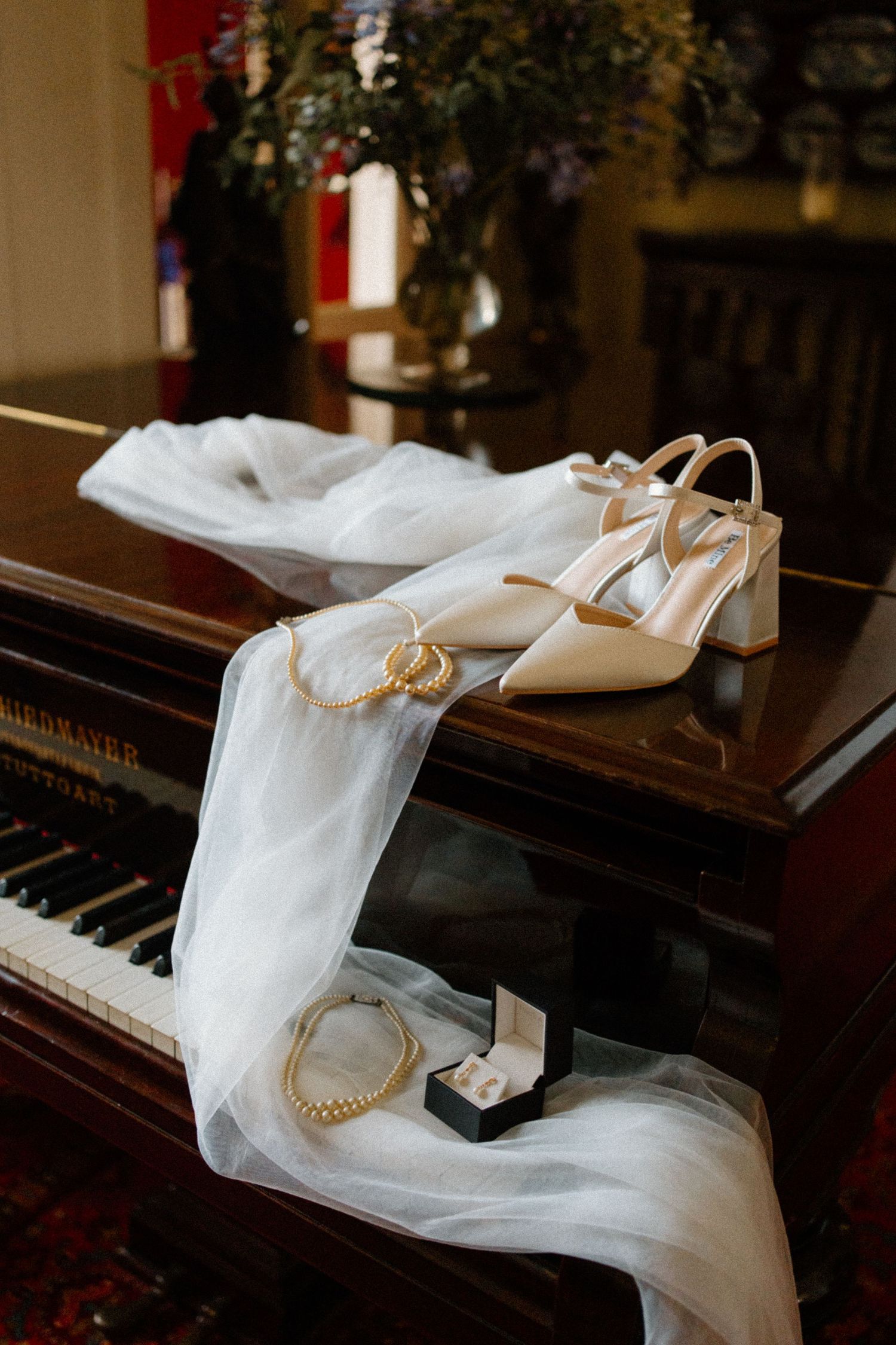Bridal accessories including white heels, veil, gold jewelry displayed on a piano.
