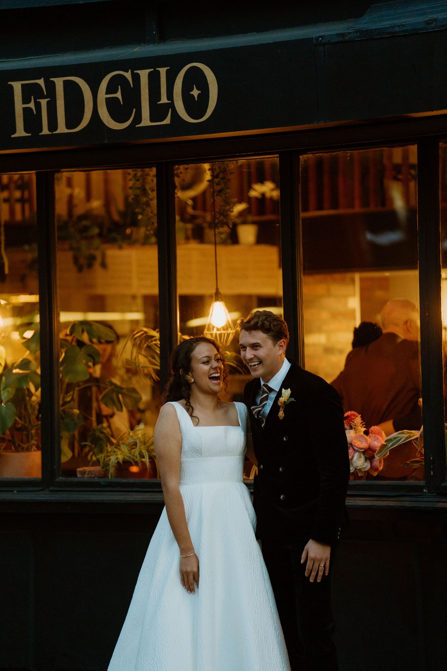 Joyful bride and groom laughing outside Fidelio restaurant during their London wedding.