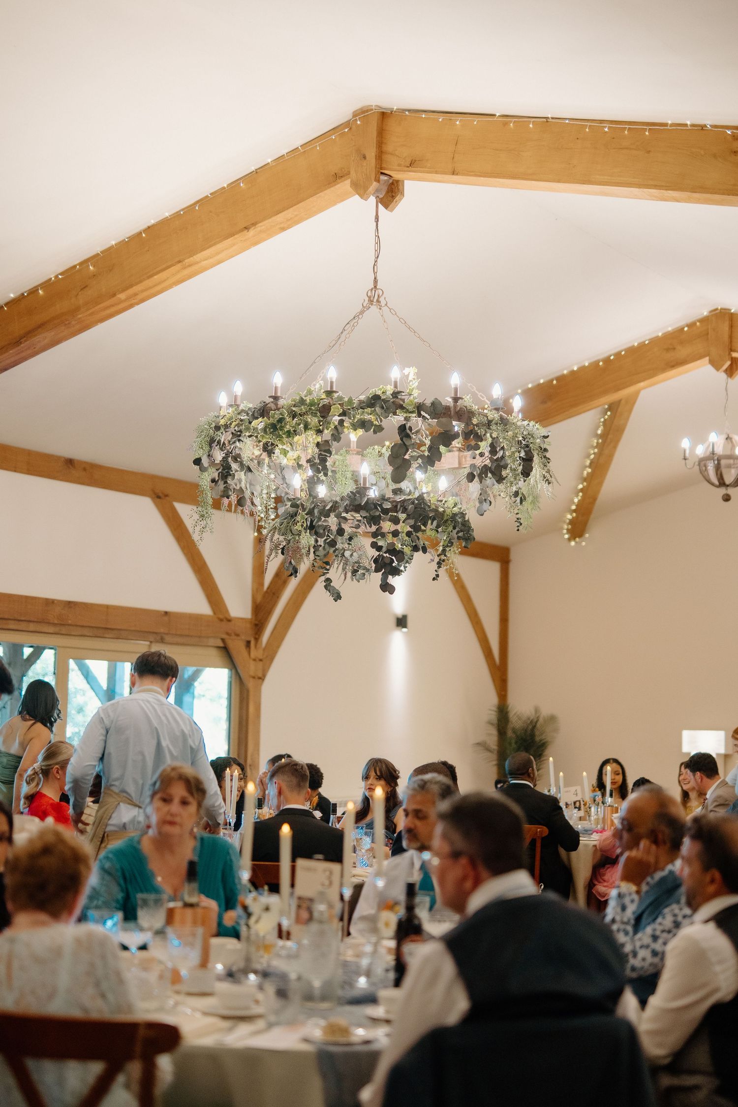 Elegant wedding reception in barn venue with floral chandelier and guests seated at round tables.