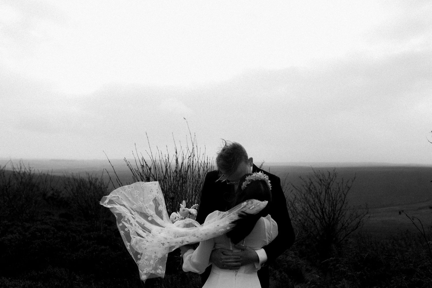 Silhouetted couple embracing on a hilltop with flowing wedding dress in the wind.