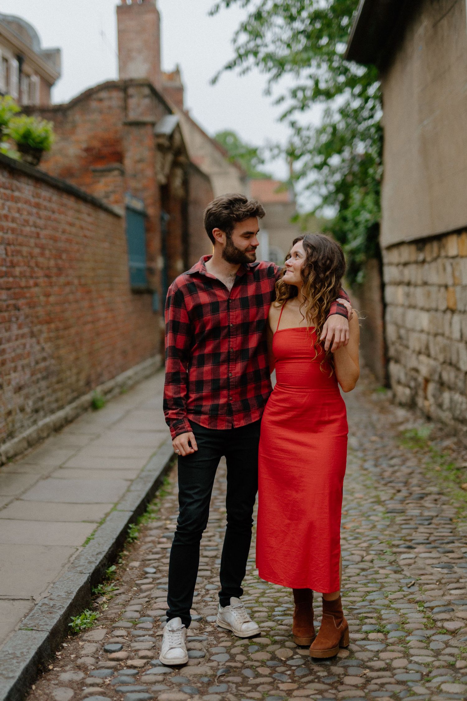 Couple walking arm in arm along a picturesque cobblestone lane with historic brick walls.