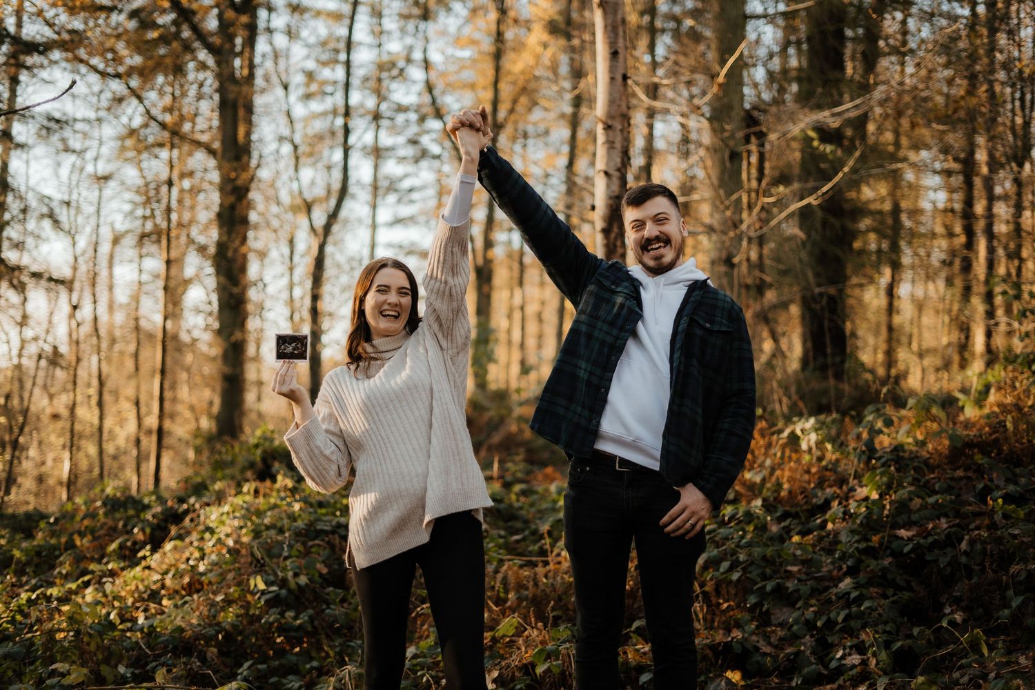 Happy couple celebrating pregnancy announcement holding ultrasound scan in autumn forest.