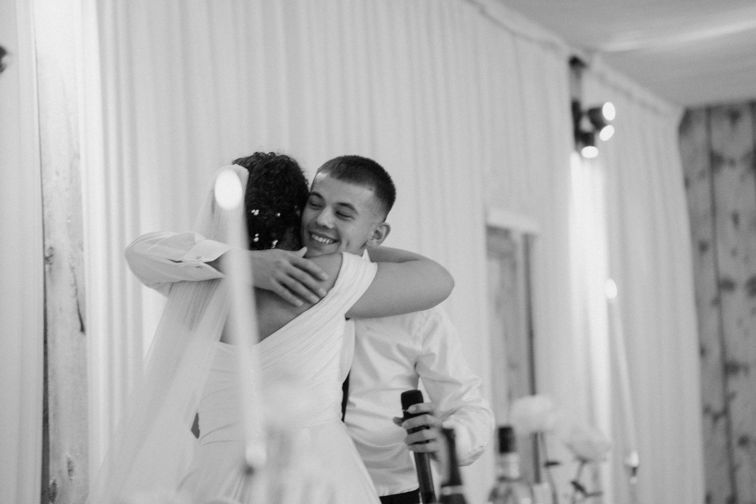 Black and white photo of bride and groom sharing a warm embrace during wedding reception celebration.