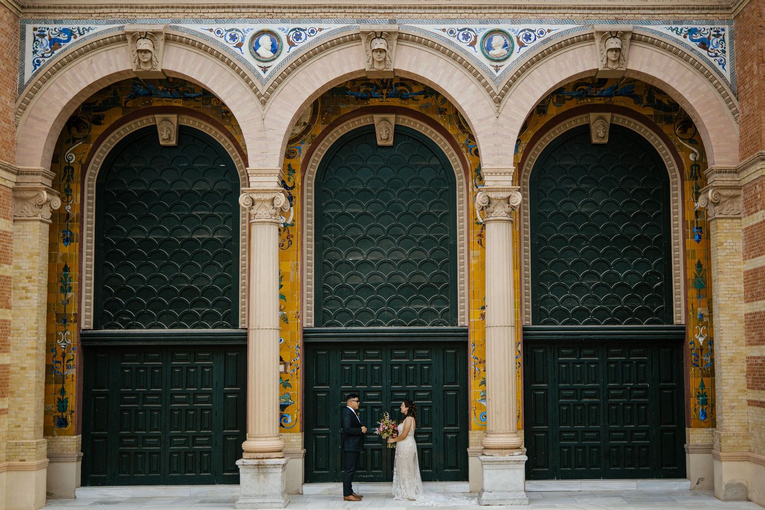Couple exchanging vows beneath ornate green arched doors of a historic building.