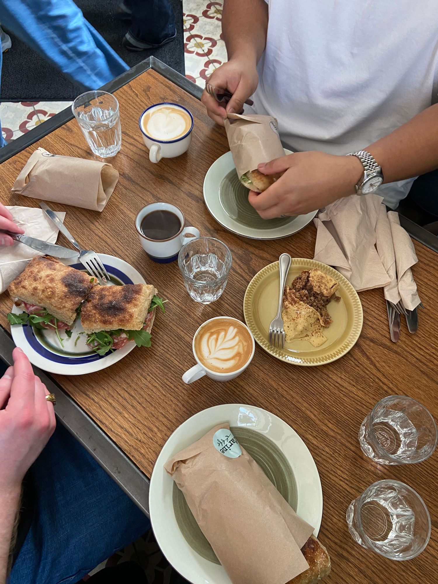 Overhead view of a cafe table with coffee drinks, sandwiches and pastries on wooden surface.