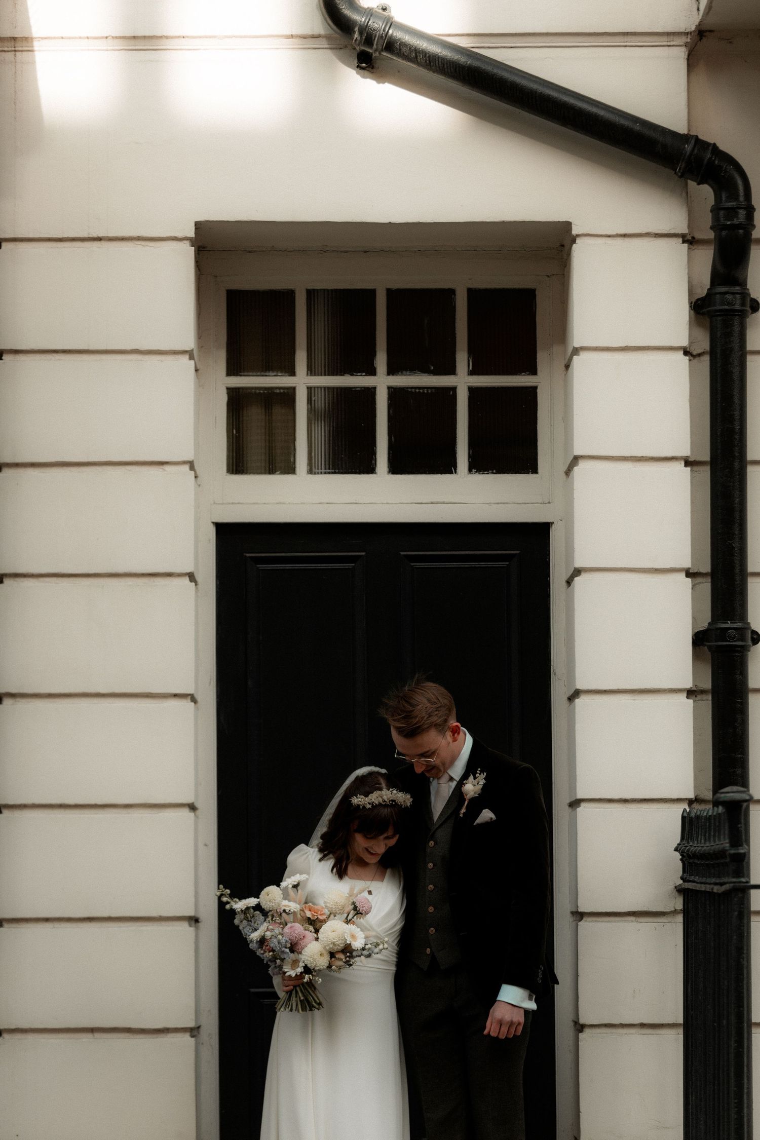 Wedding couple framed in architectural doorway holding white floral bouquet.