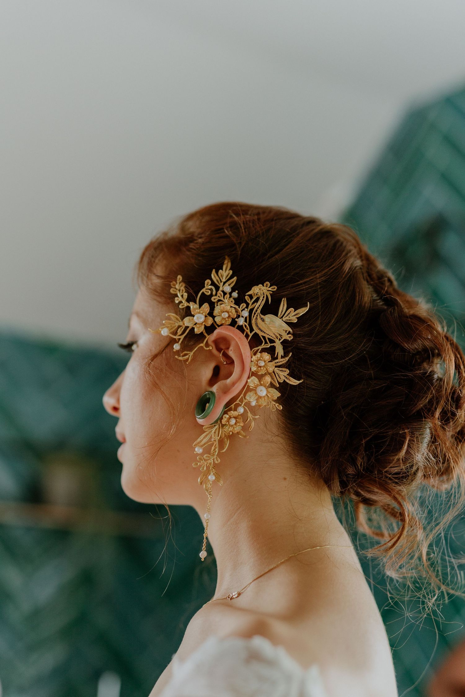 Close-up profile of bride wearing an ornate gold floral hair comb and matching earrings.