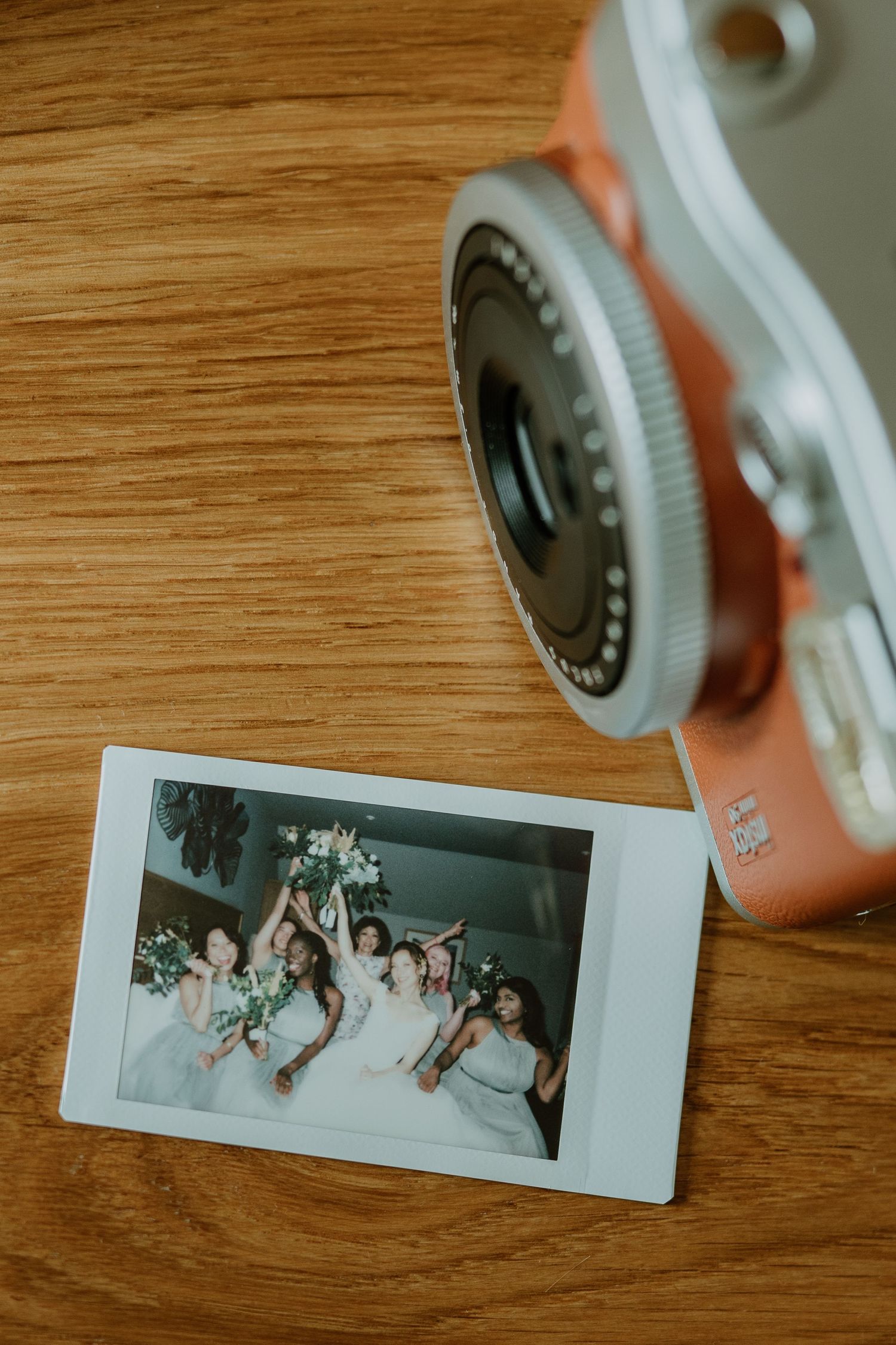 Instax polaroid photo of bridesmaids tossing bouquet captured beside a pink instant camera.