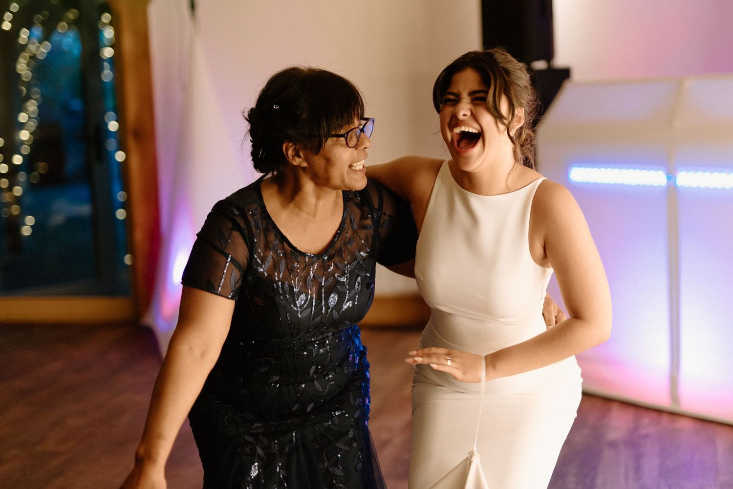 Bride and older woman laughing together joyfully on the wedding reception dance floor.