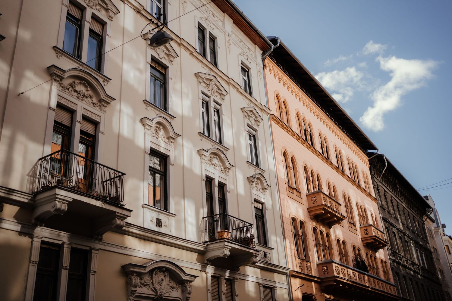Historic European apartment buildings with decorative facades and wrought iron balconies in warm sunlight.