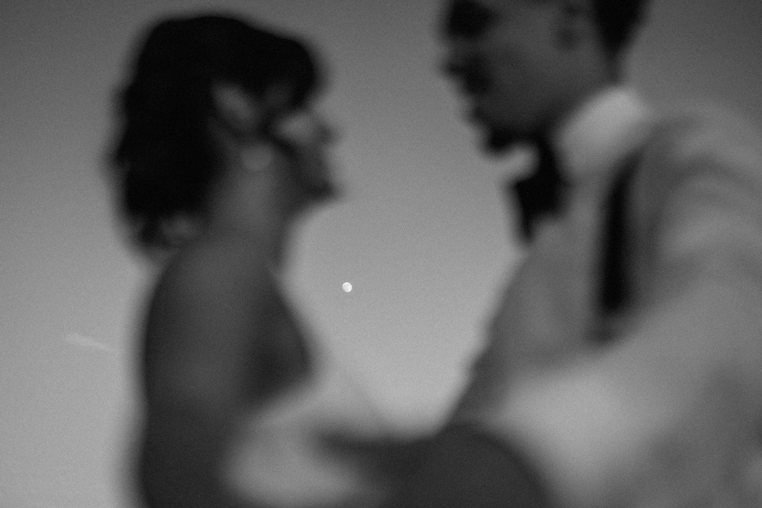 Blurry black and white photo of a bride and groom sharing an intimate moment with a bokeh light between them.