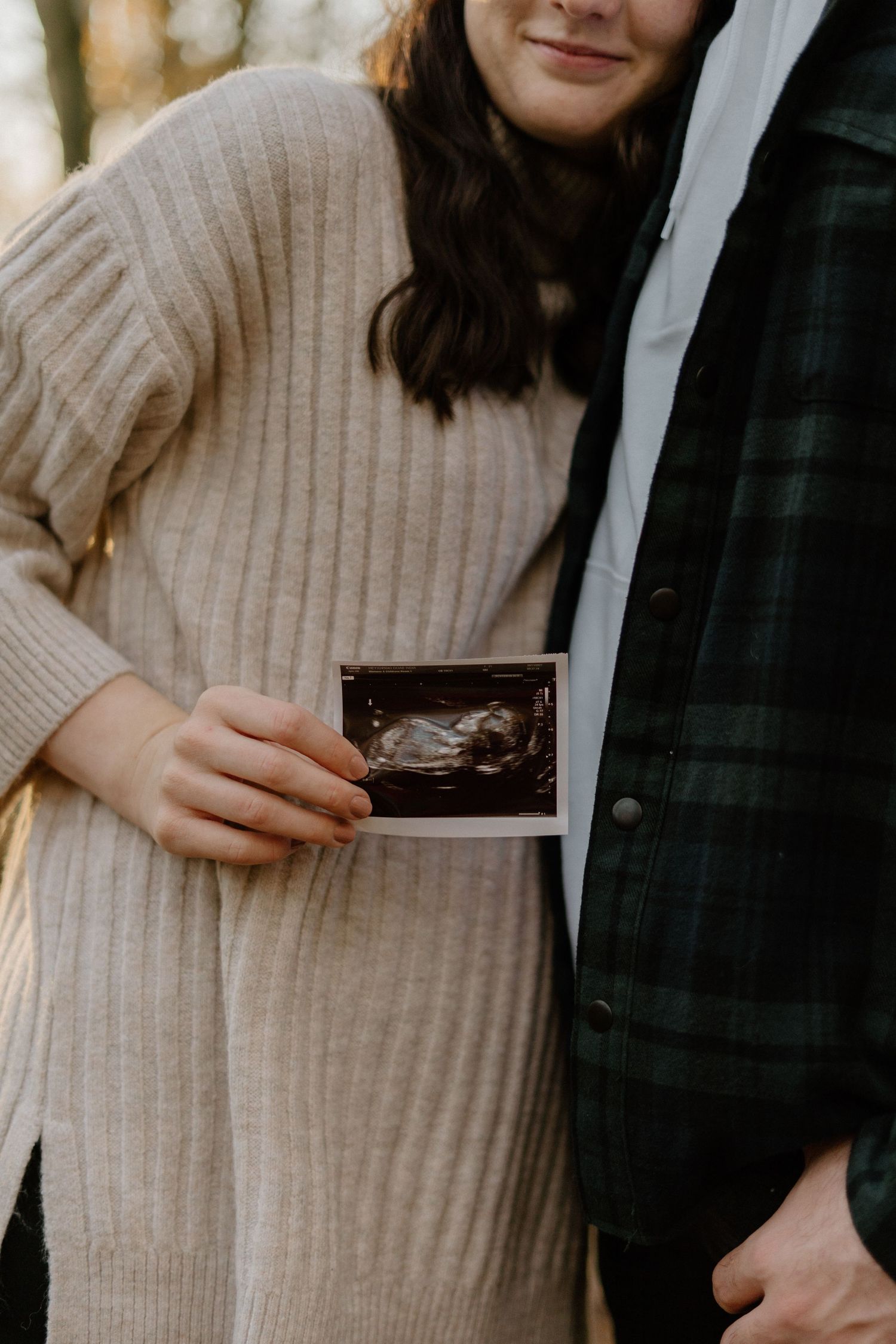 Expectant couple holding ultrasound scan photo in warm autumn woodland setting.