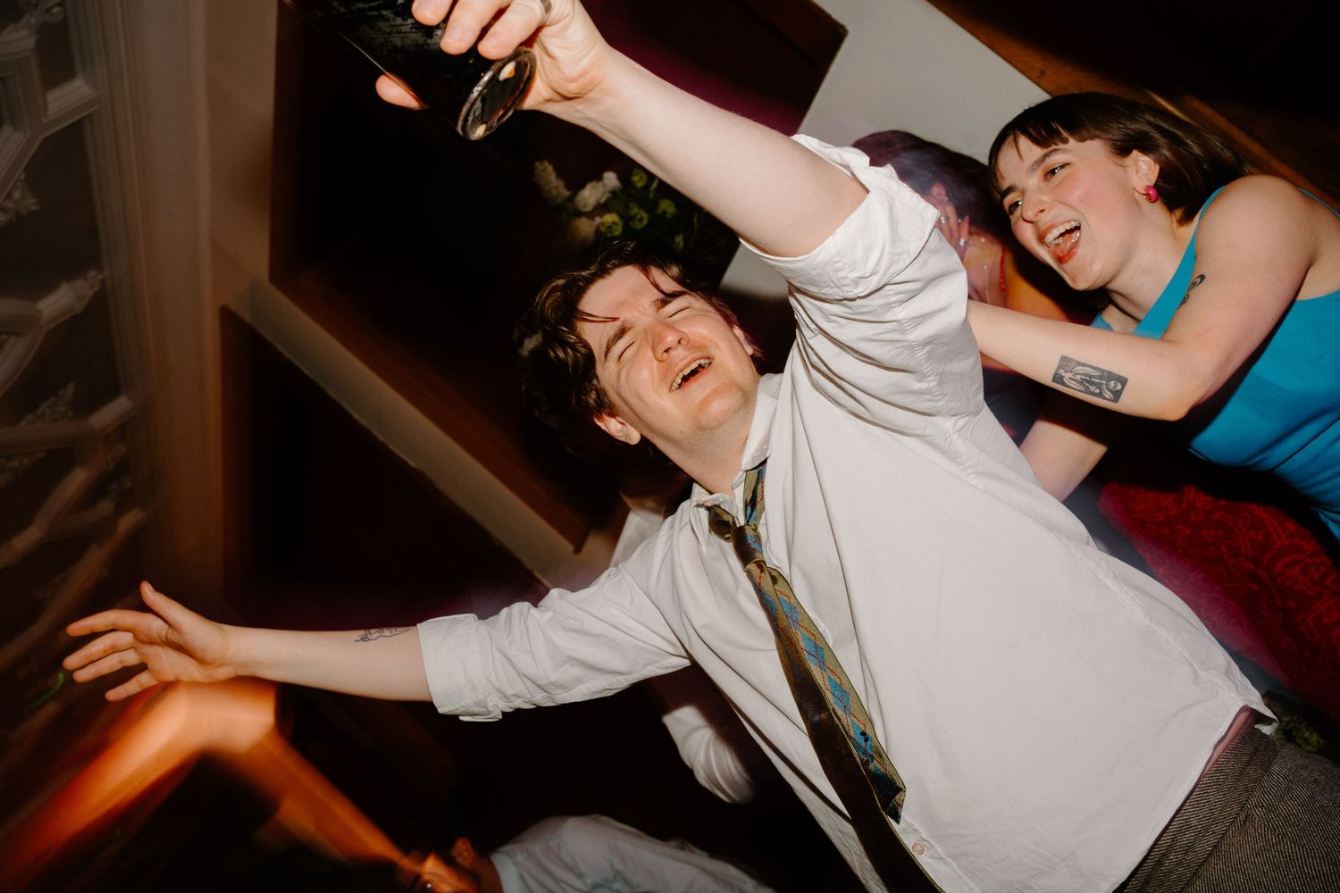 Enthusiastic wedding guest dances energetically holding bottle aloft at fun late-night wedding party.