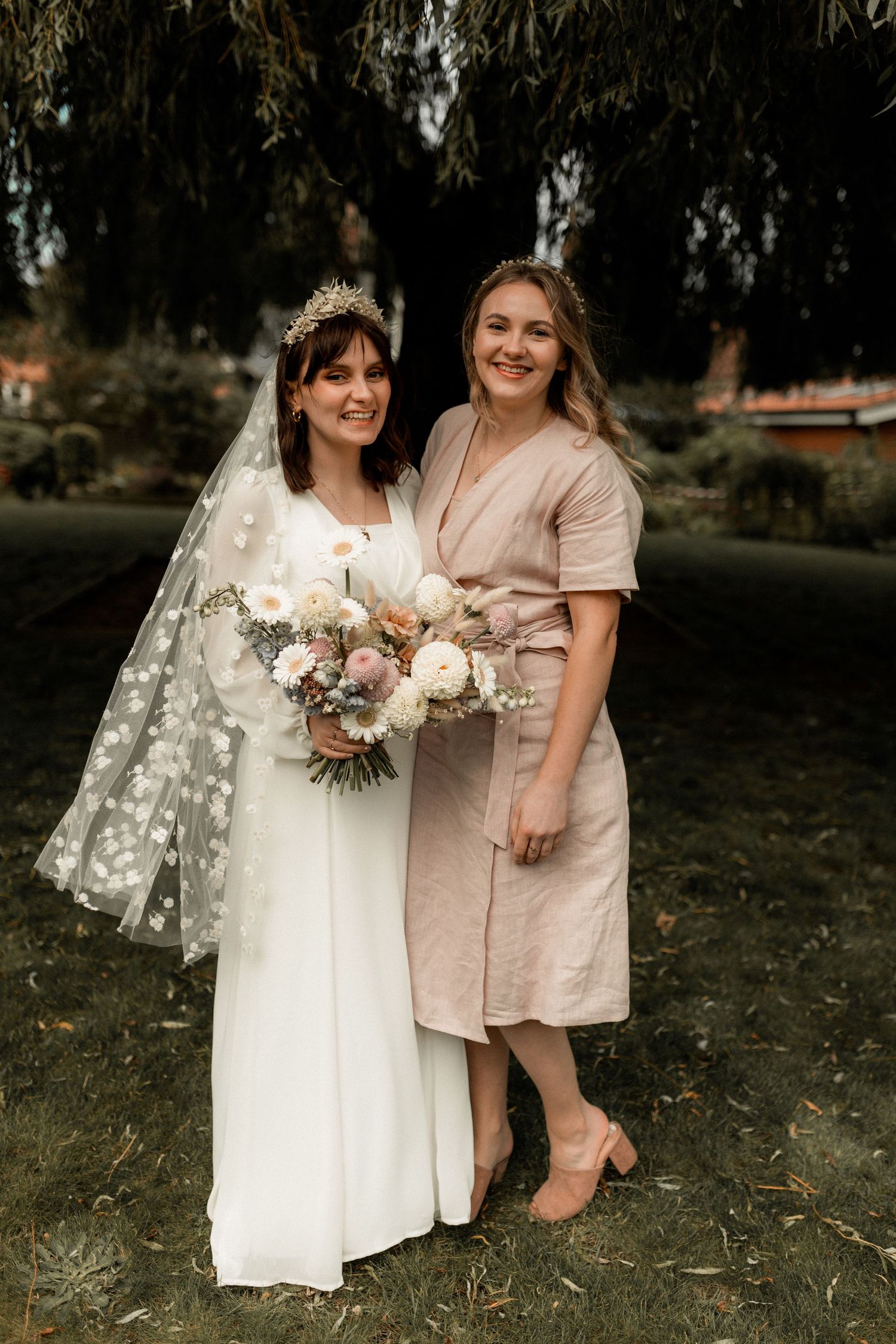 A wedding portrait featuring elegant dresses and a beautiful floral bouquet under willow trees.