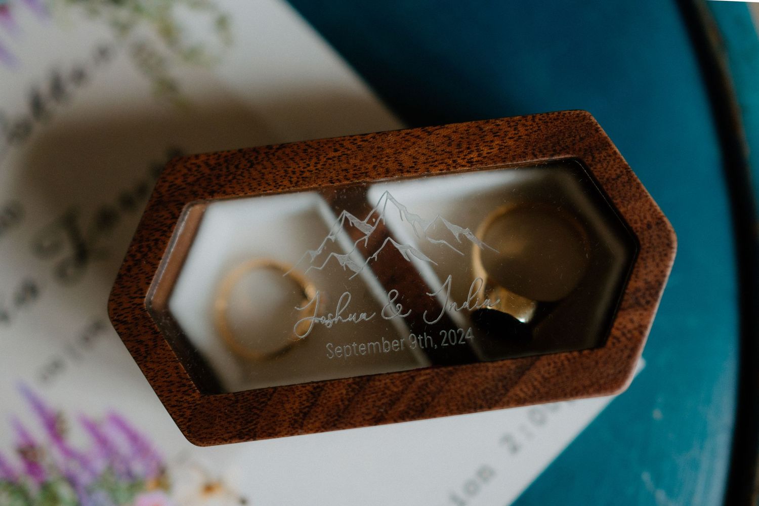 Wedding rings rest in an elegant wooden hexagonal box lined with white padding.
