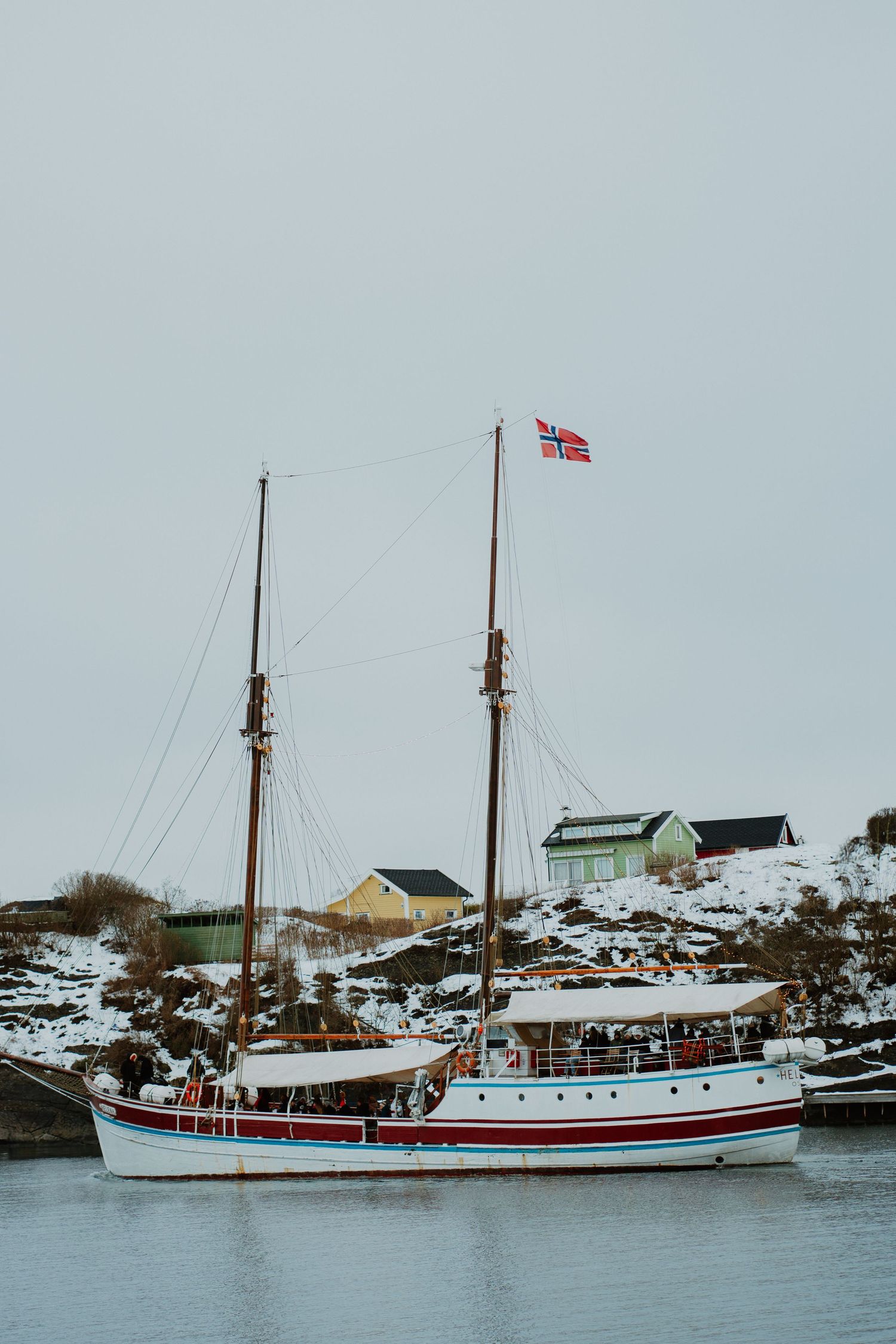 Traditional Norwegian sailing vessel with red and white hull flying Norwegian flag in snowy harbor.