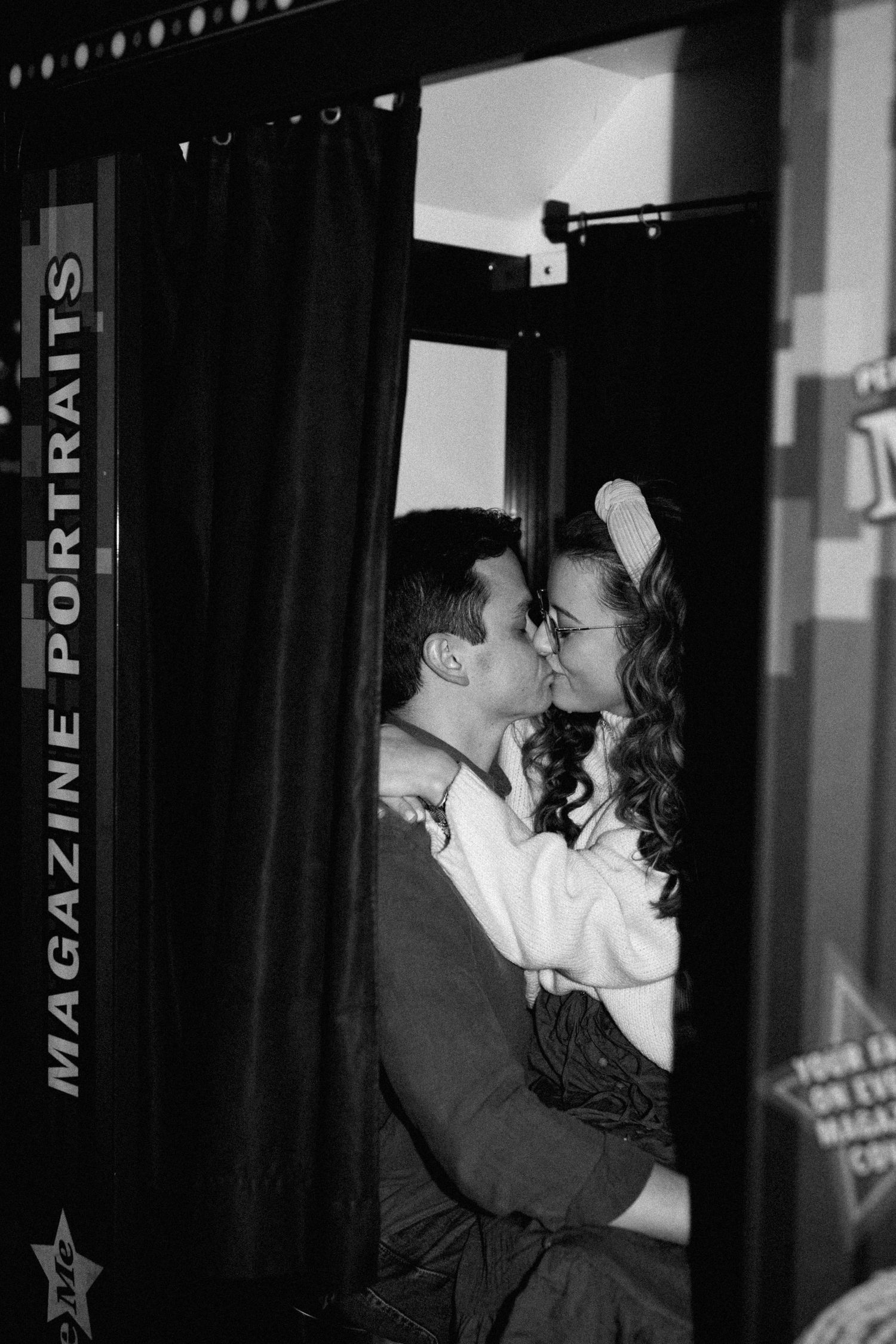 Couple sharing a romantic kiss inside a vintage photo booth with Magazine Portraits signage.