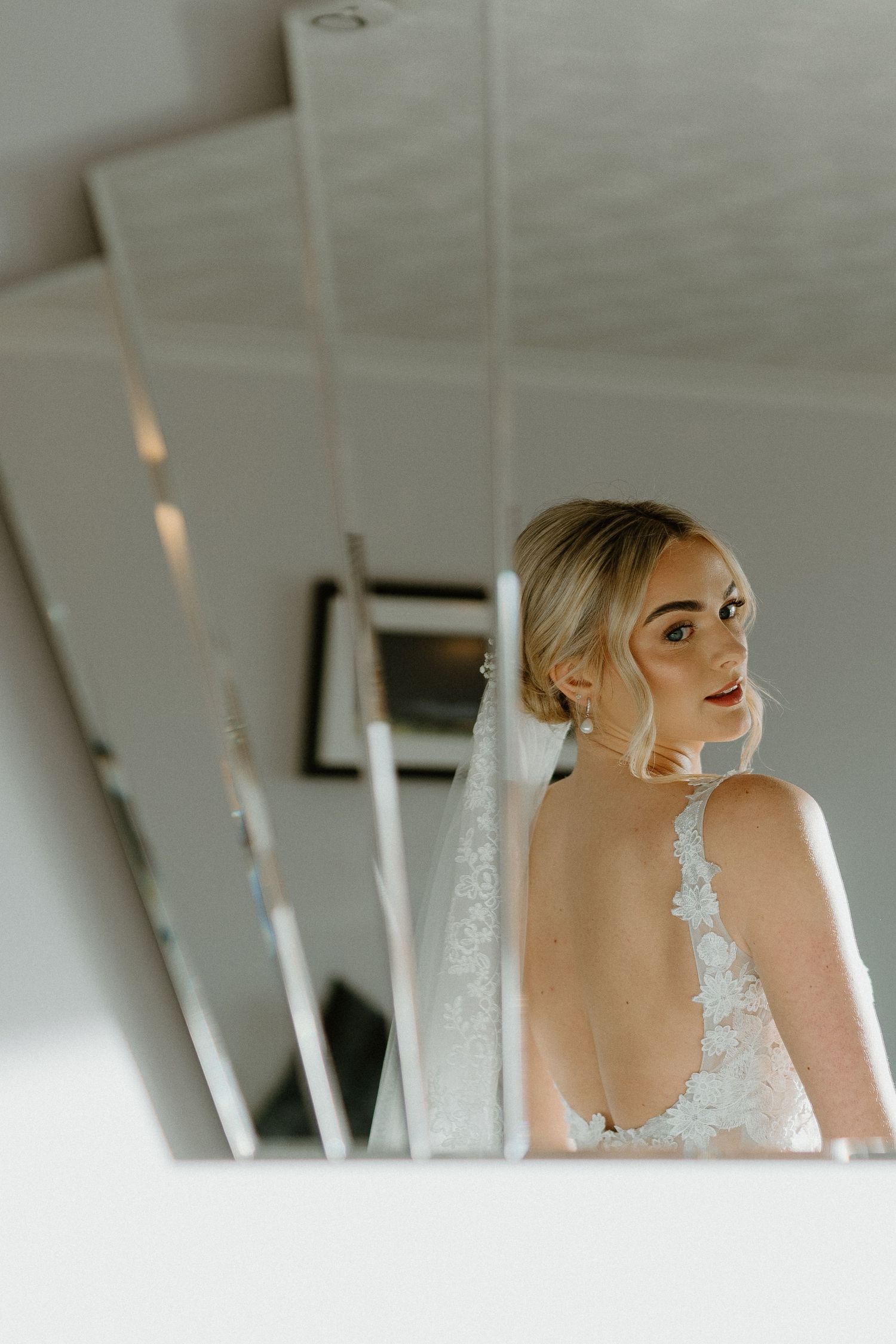 Bride in backless lace wedding gown with veil reflected in multiple mirrors.