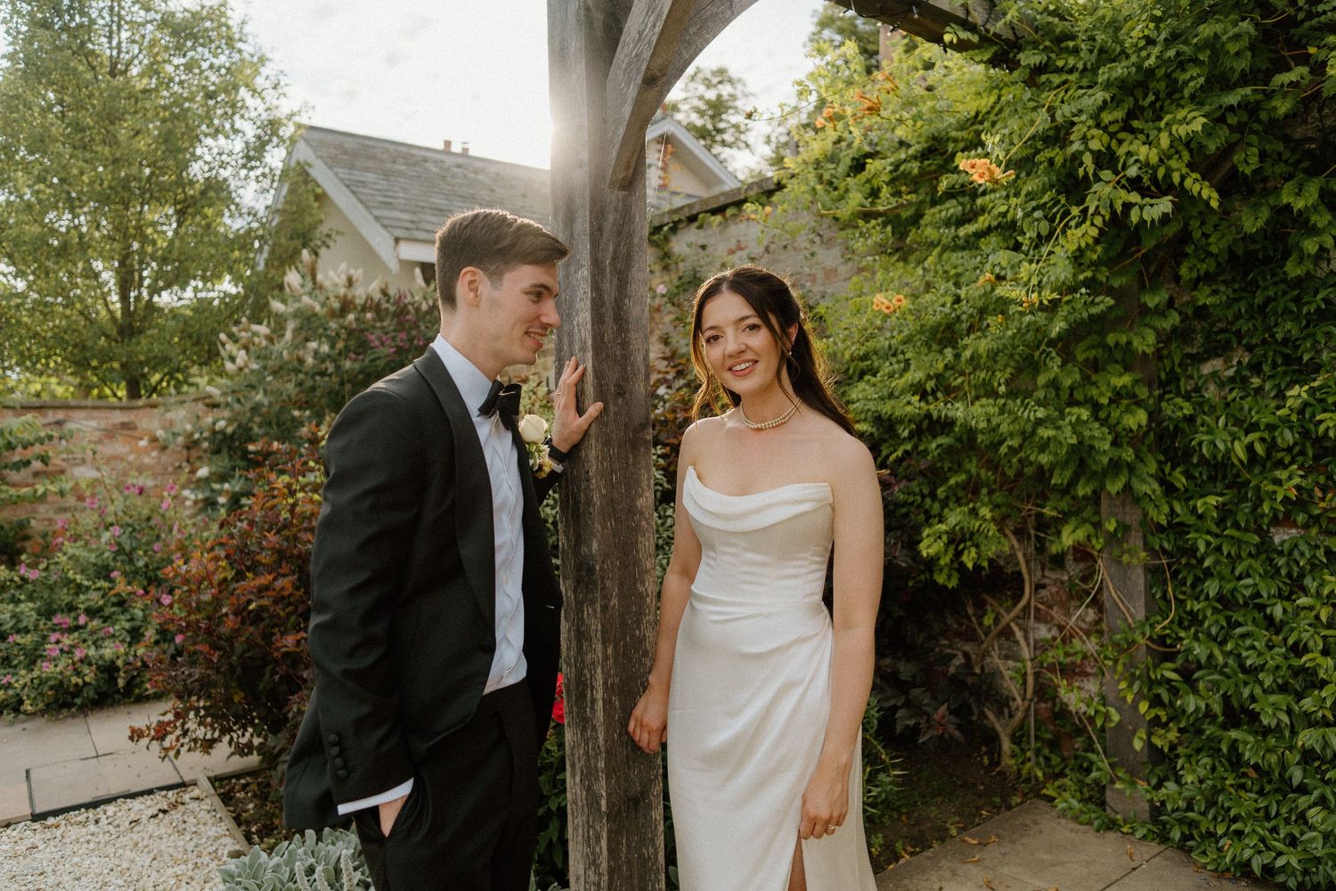 Bride and groom sharing a romantic moment by a rustic wooden post in a garden.