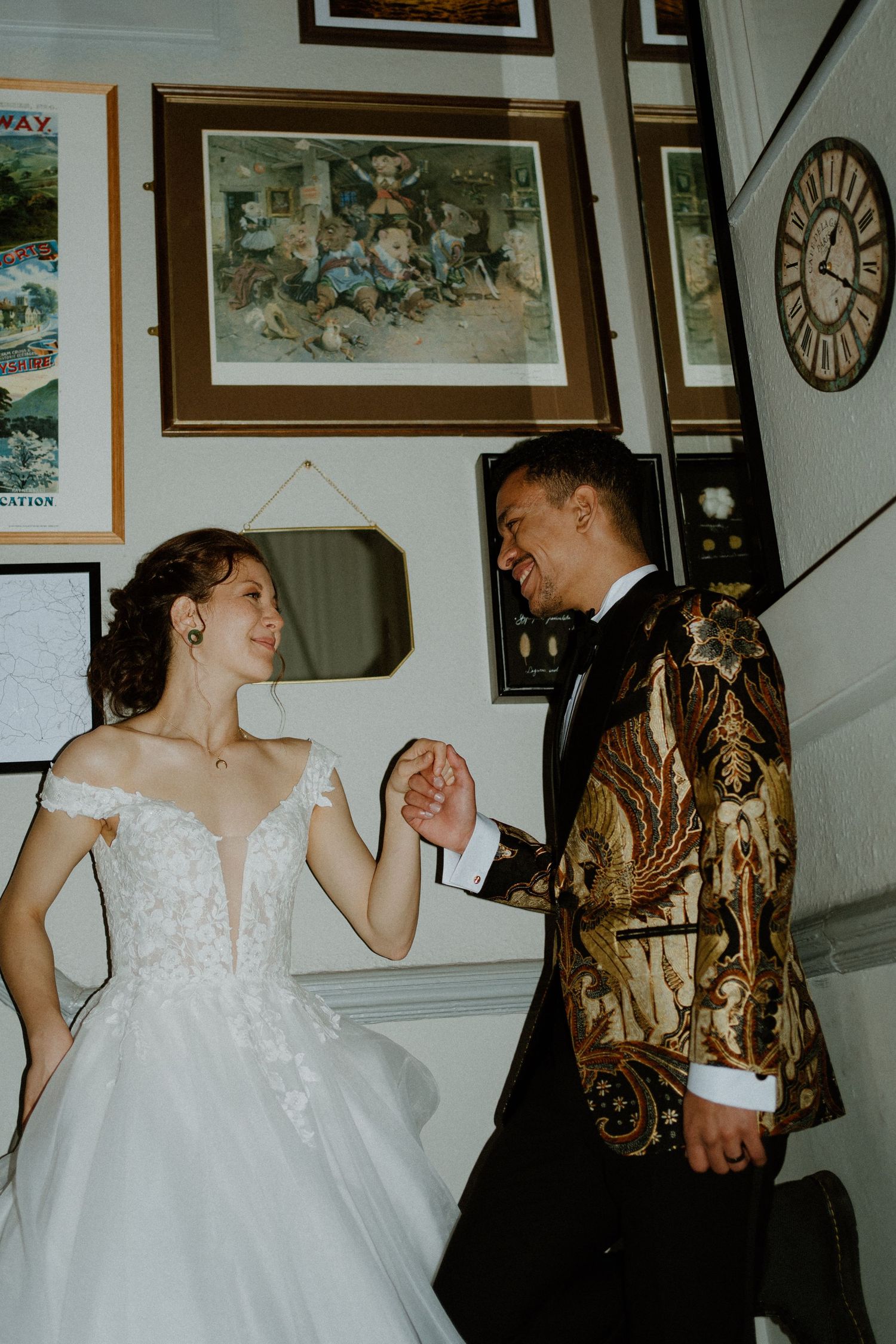 Bride and groom share a joyful moment indoors, groom in gold batik blazer holding bride's hand.