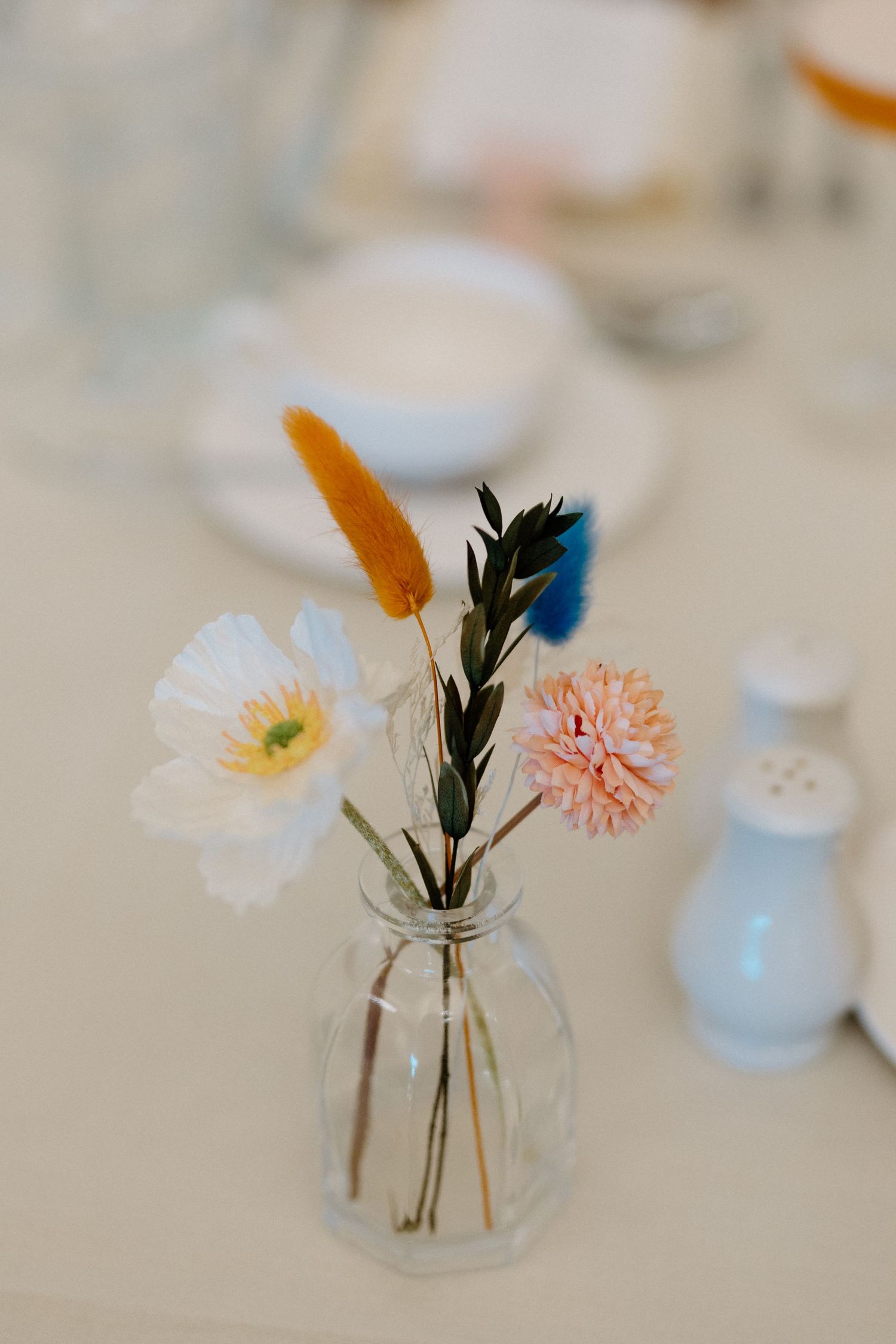 Delicate small glass vase with white poppy, pink carnation, and blue feather as table centerpiece.