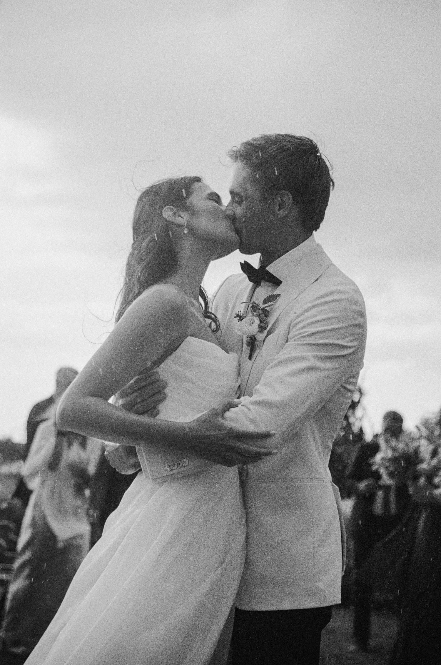 Bride and groom sharing first kiss in black and white outdoor wedding photo.