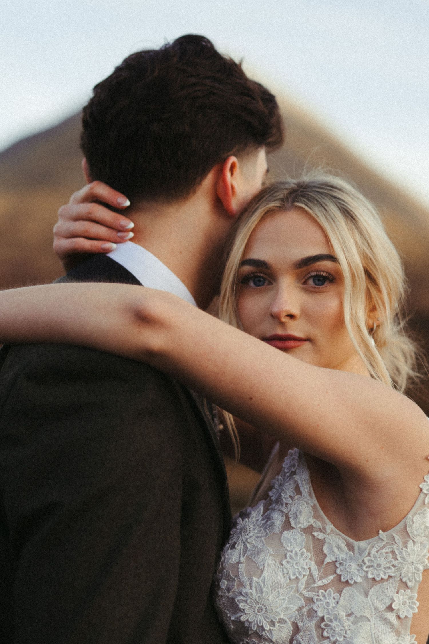 Bride in lace gown embraces groom outdoors with misty mountains in background at scenic elopement.