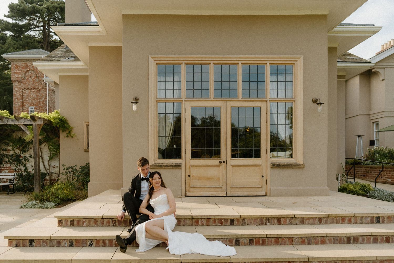 Bride and groom sitting on steps of elegant venue exterior for wedding portrait.