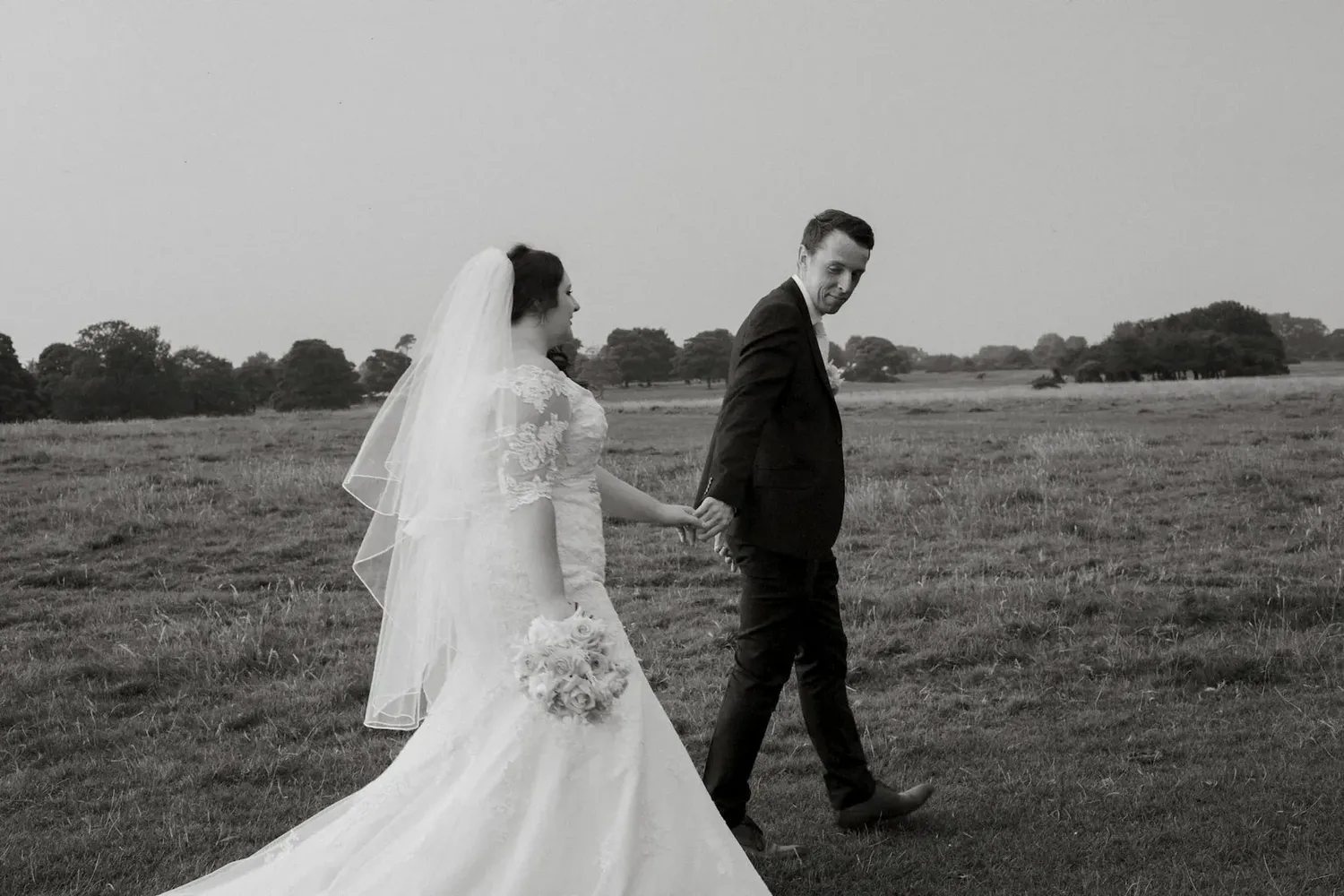 Black and white photo of newlyweds walking through a meadow.