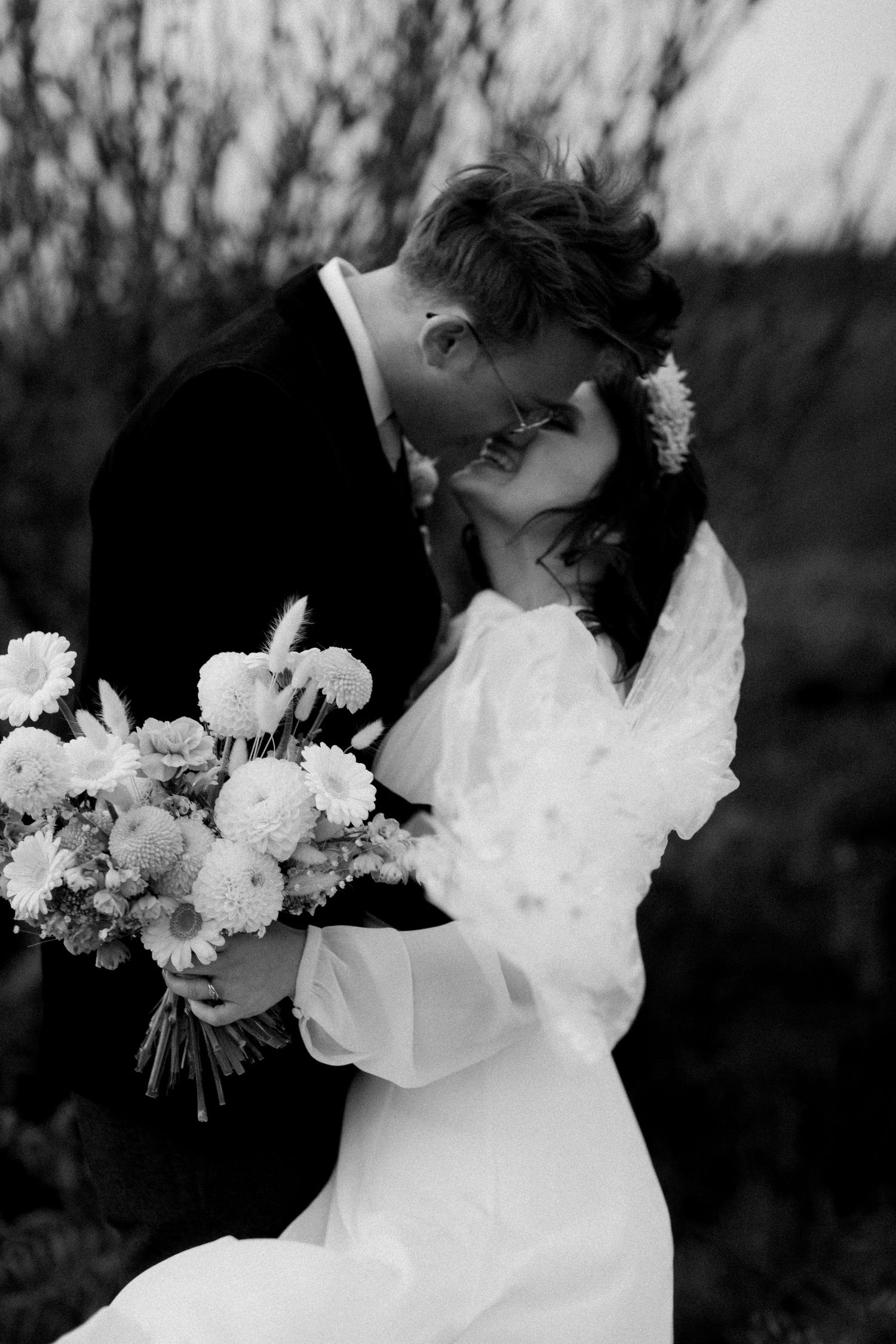 Black and white photo of newlyweds sharing an intimate moment with white floral bouquet.