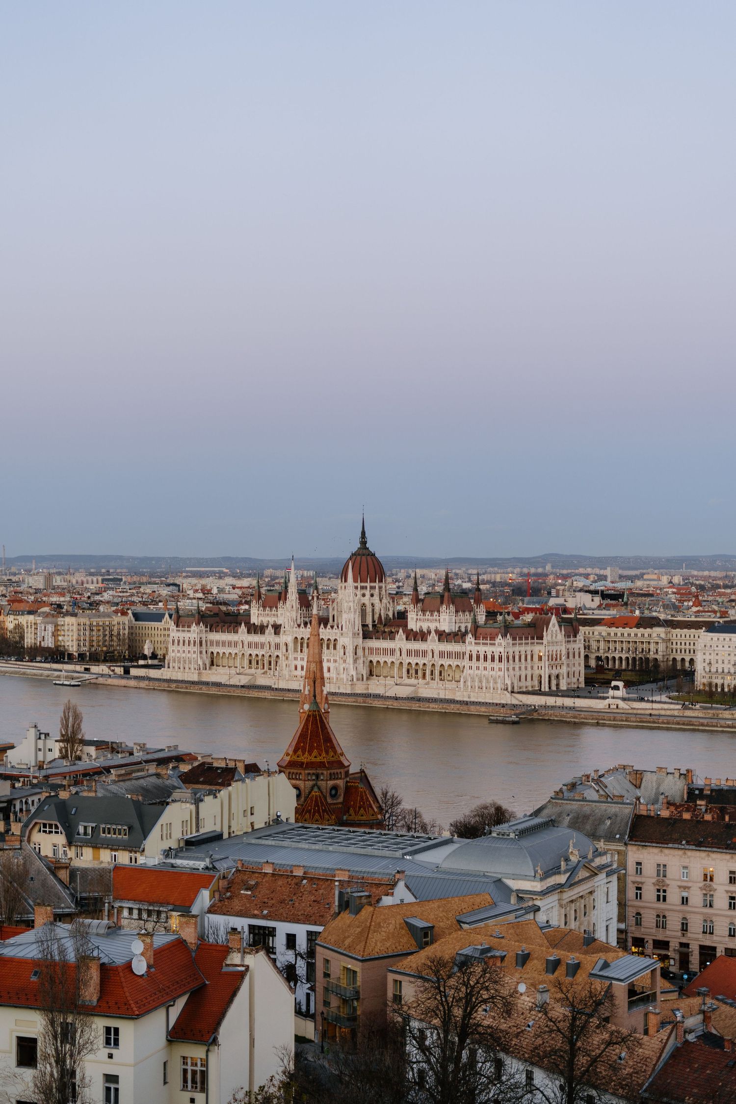 Aerial view of Budapest's iconic Parliament Building along the Danube River with historic cityscape at sunset.