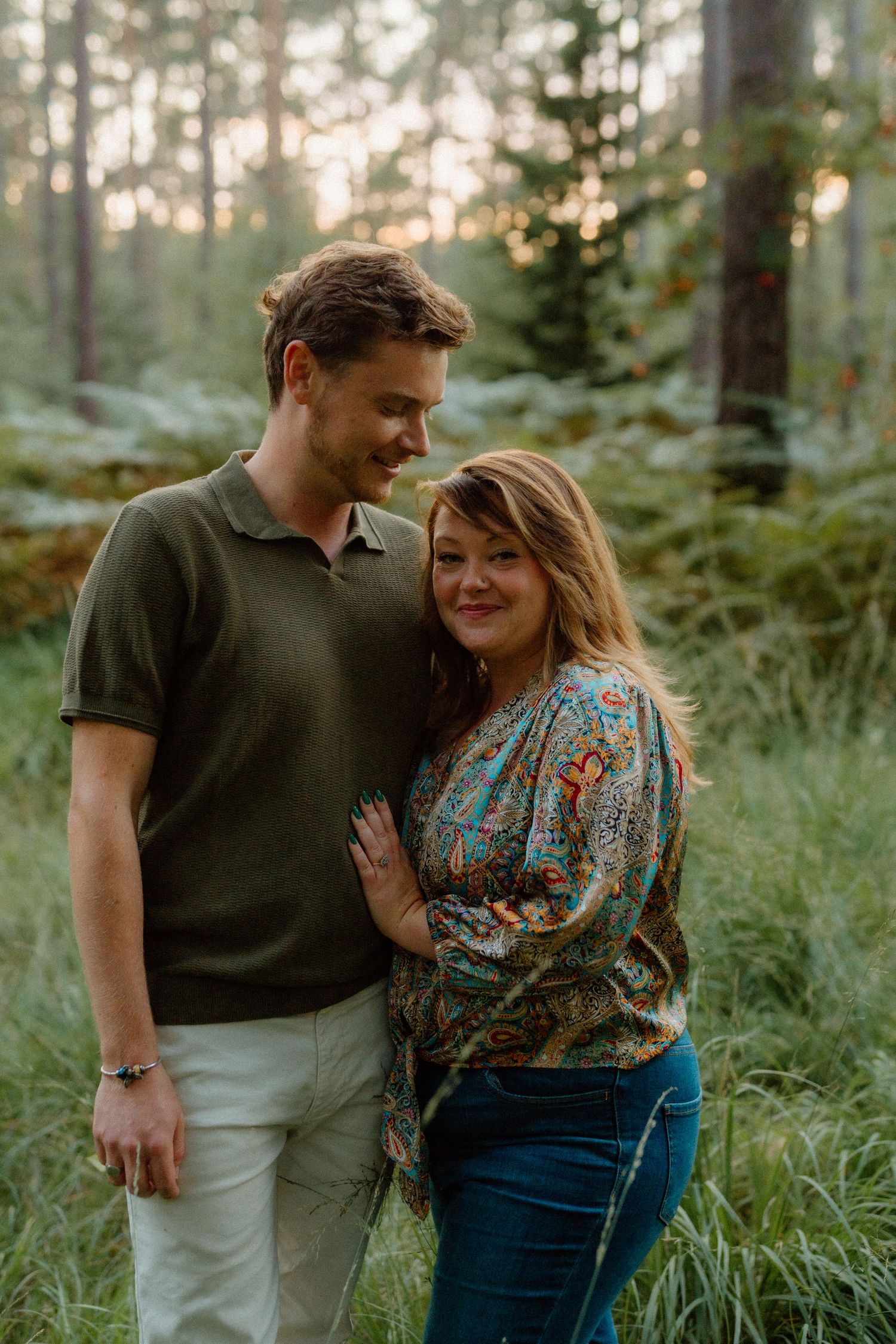 A couple sharing an intimate moment in a forest during golden hour with sunlight filtering through trees.