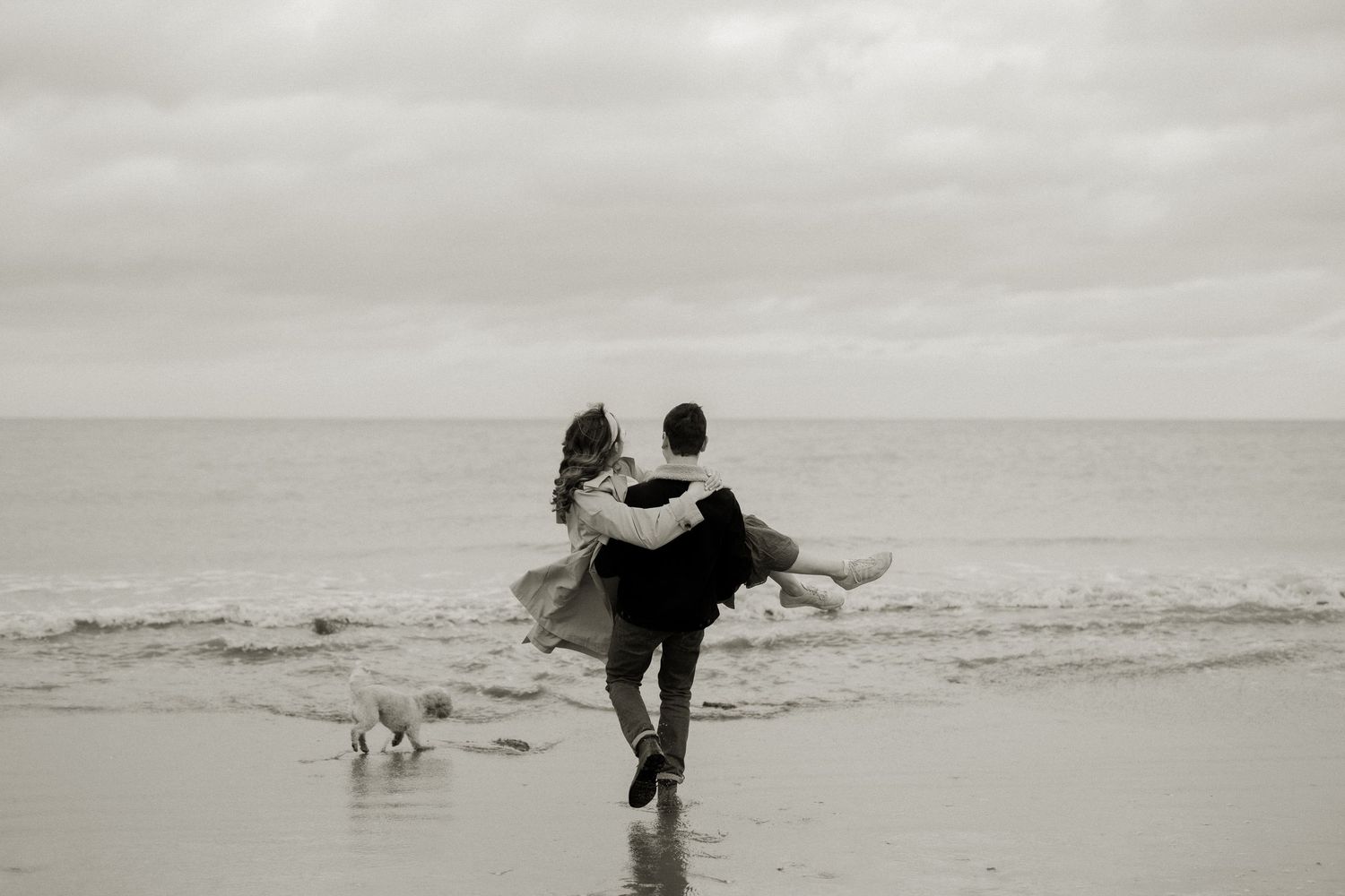 Couple sharing romantic moment on beach, groom carrying bride in wedding attire by the ocean.