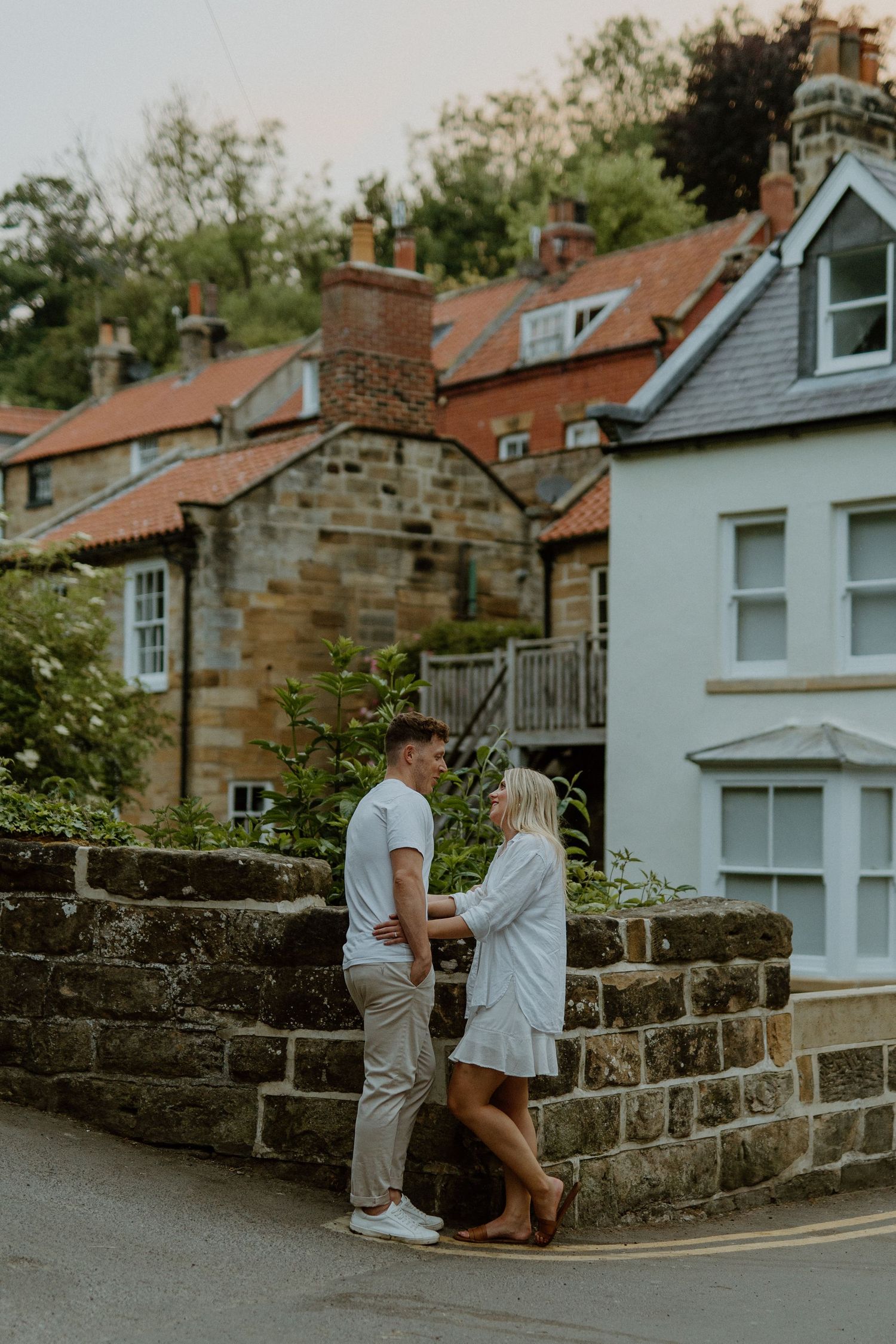 Couple facing each other tenderly beside a stone wall in a charming village street.
