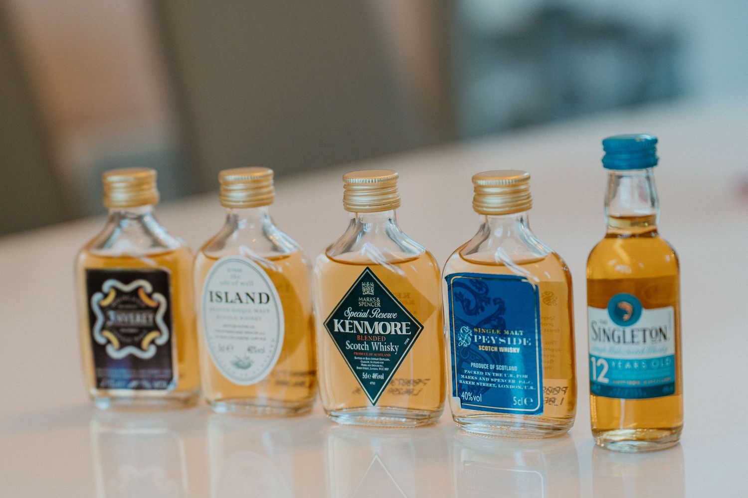 Five miniature whisky bottles lined up on white surface including Kenmore and Singleton.