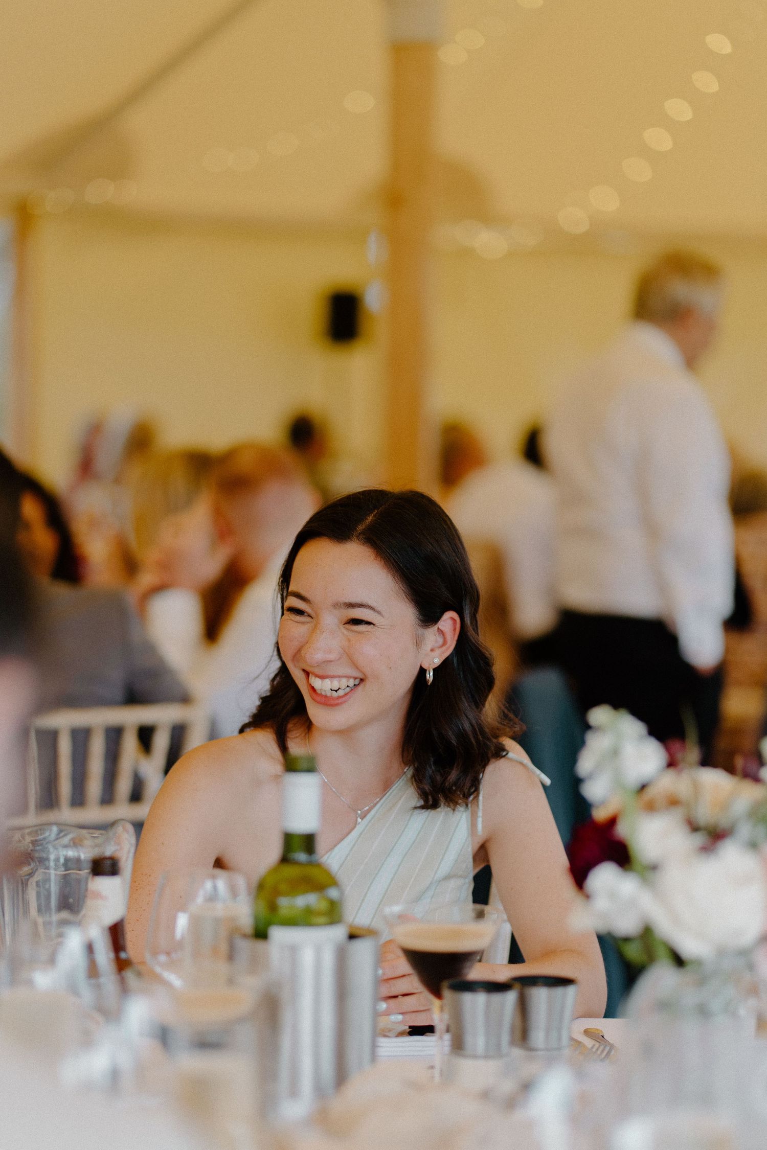 Laughing wedding guest in white dress seated at elegant reception table inside a marquee tent.