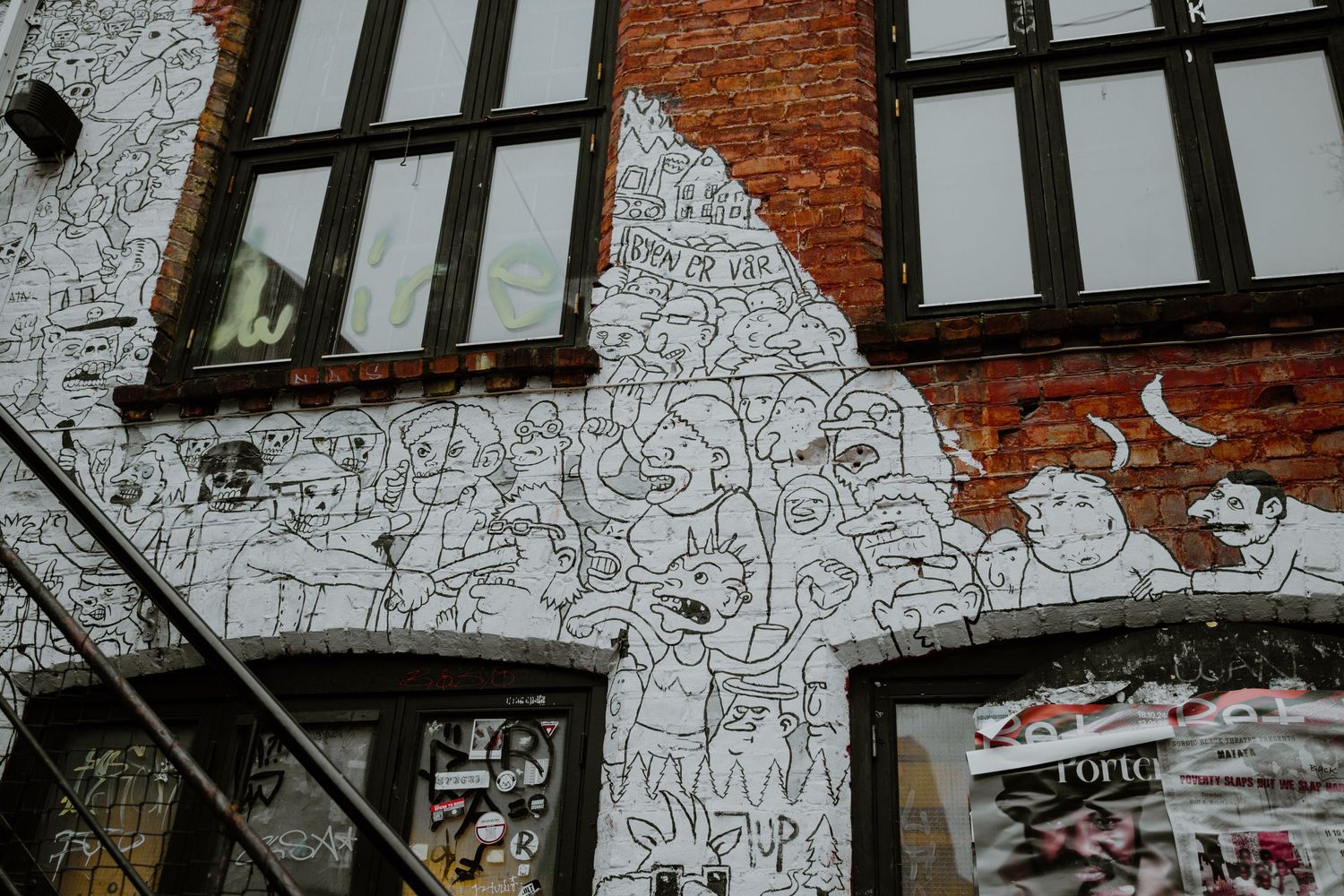 Black and white line art mural covers the exterior wall of a brick building with Tudor-style windows.