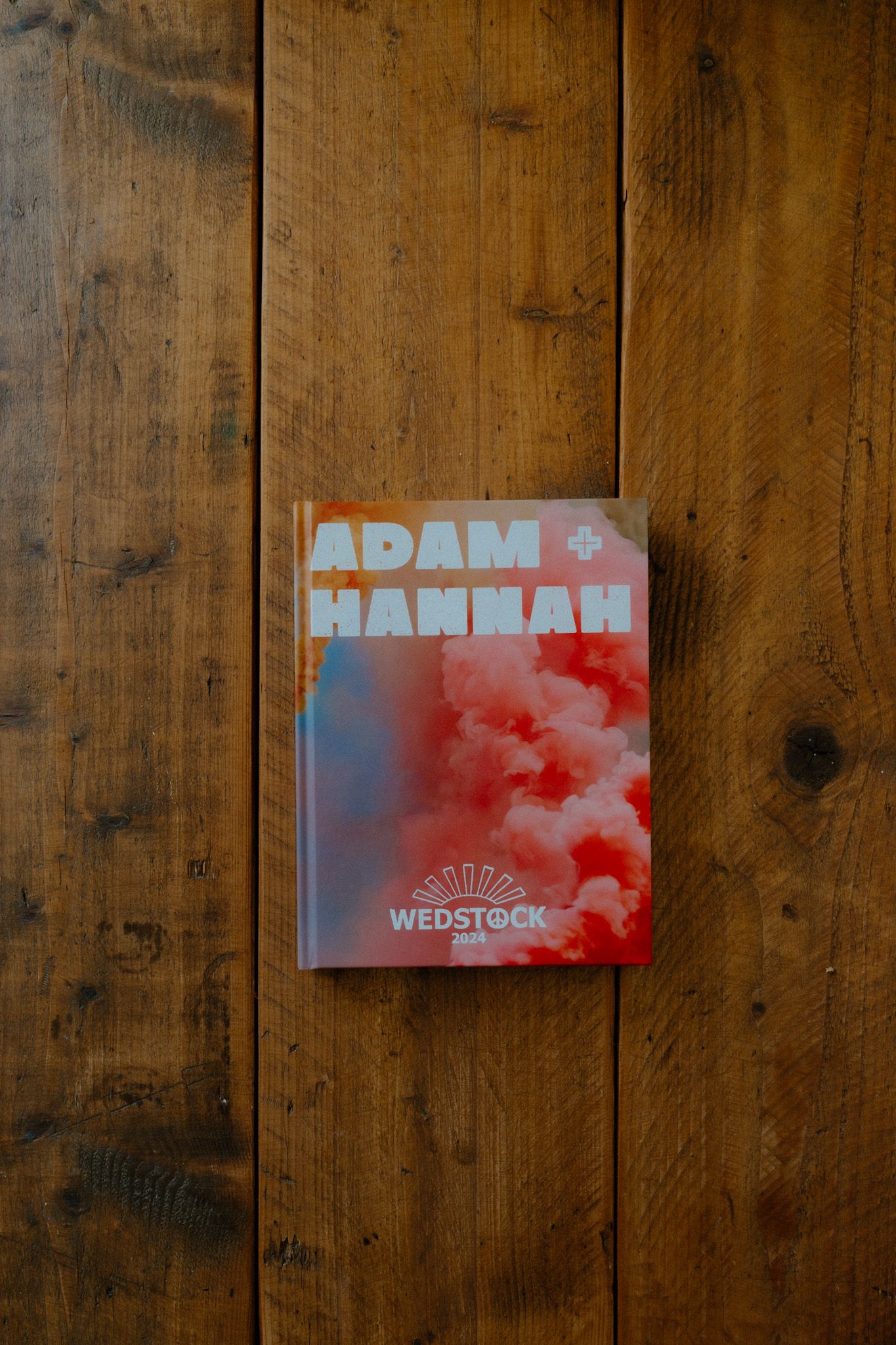 Pink and blue wedding invitation card with the text 'Adam + hannah' lies on a rustic wooden surface.