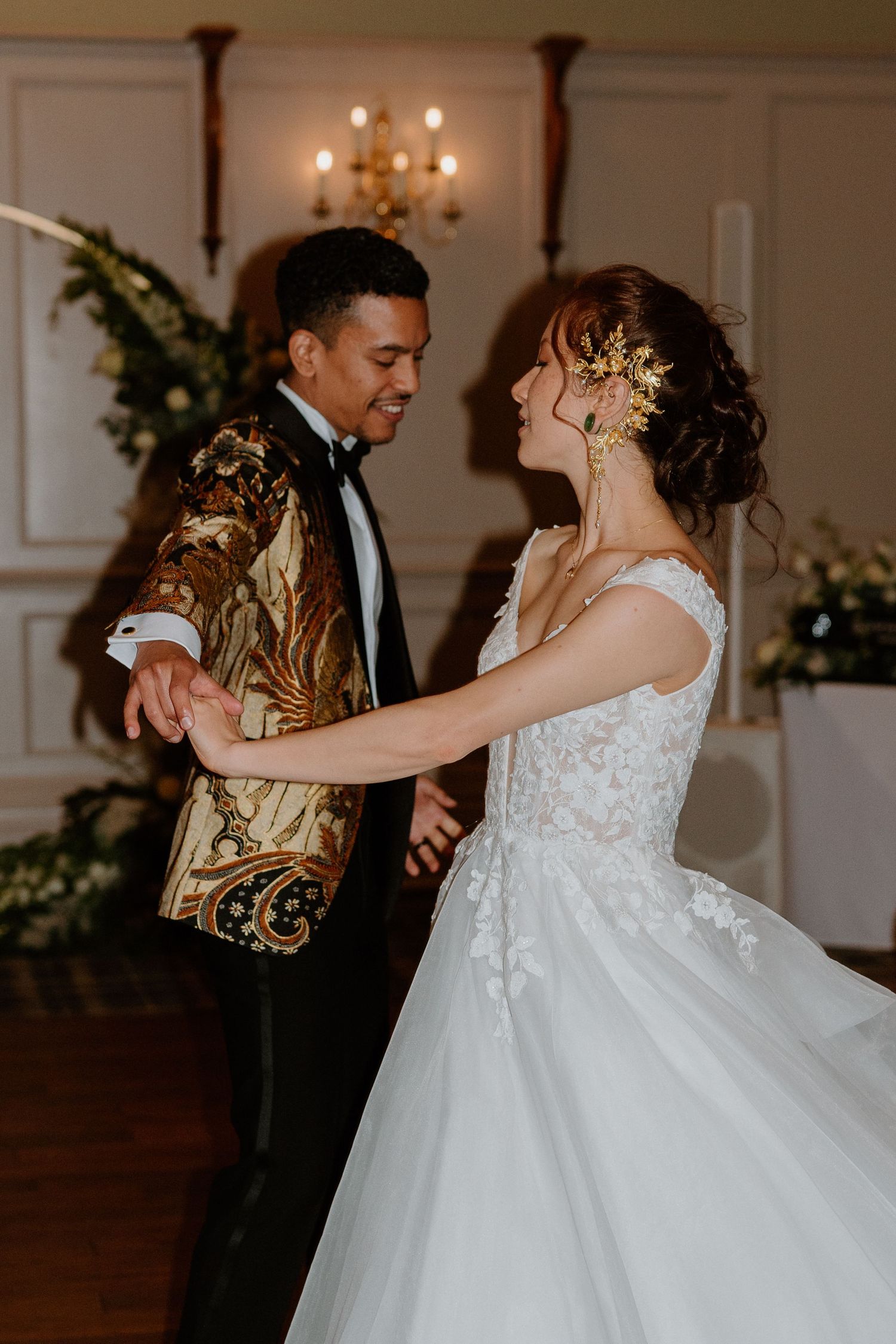 Bride and groom share first dance, bride wearing gold hair accessories and lace ballgown in elegant venue.