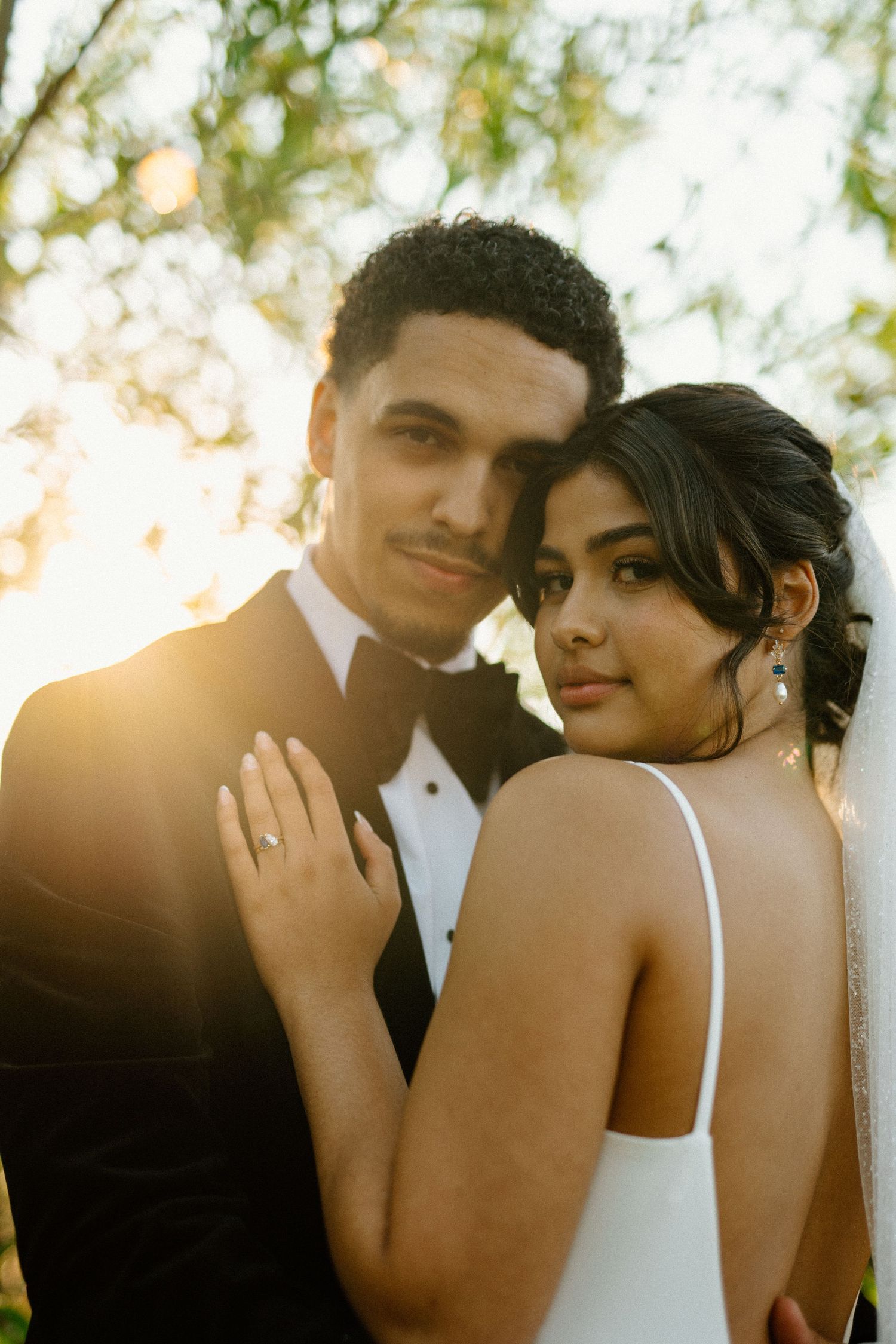 Newlywed couple posing together at golden hour, bride in white gown and groom in black tuxedo.