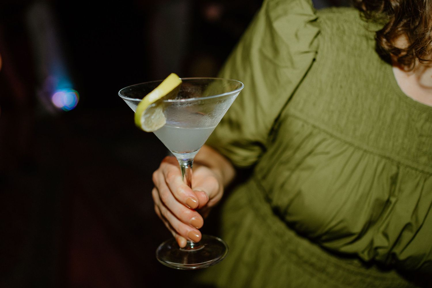Guest in green dress holding a classic martini cocktail at a wedding reception.