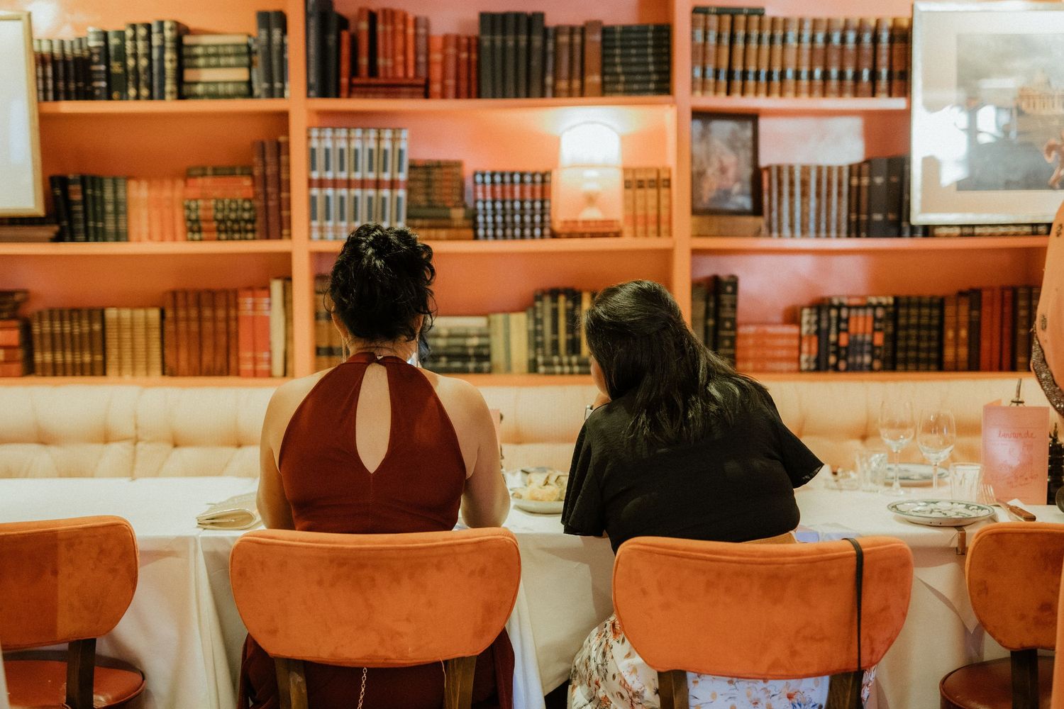 Two women seated at a elegantly set dining table in front of a bookshelf.