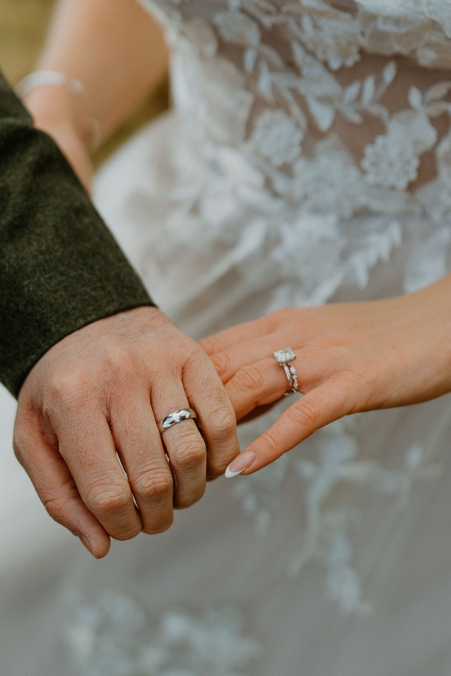 Close-up of bride and groom hands showing wedding rings, bride wearing diamond engagement ring.