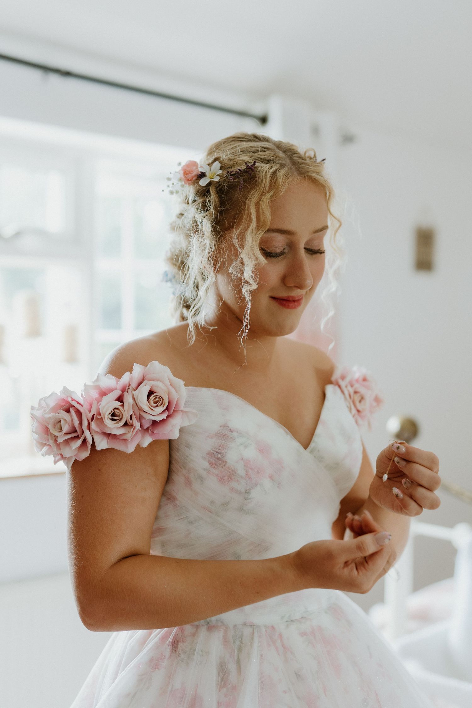 Bride in floral off-shoulder wedding dress with pink roses adjusting her bracelet before the ceremony.