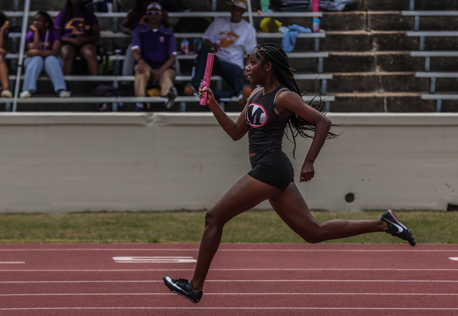 Female athlete sprinting on a track while holding a pink relay baton during a race.