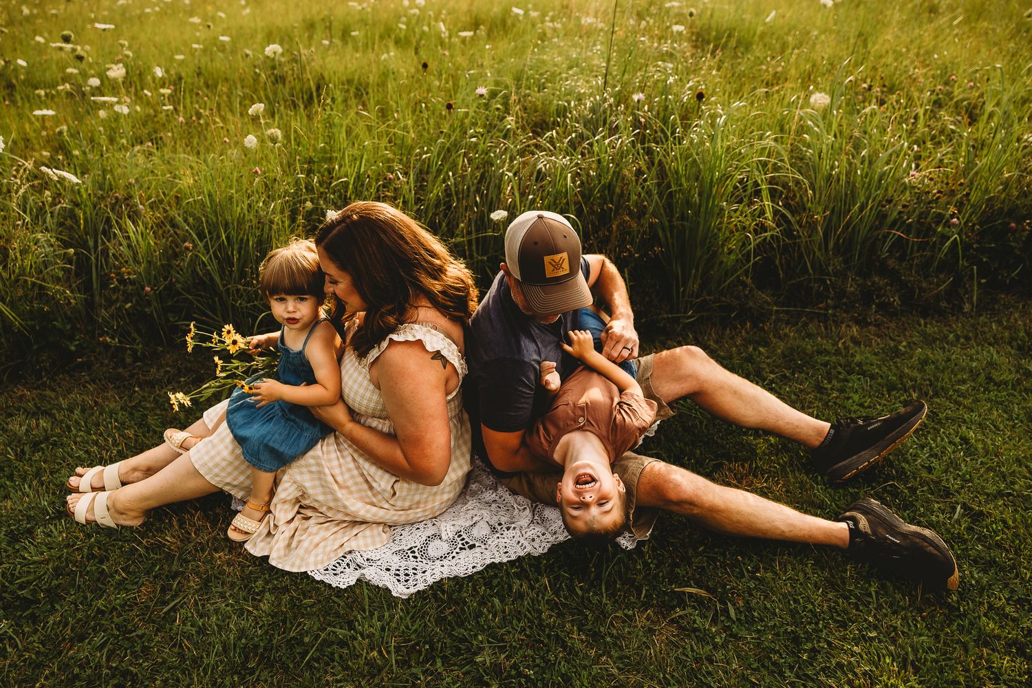 Relaxed family sitting together on blanket in wildflower meadow during warm golden hour light.