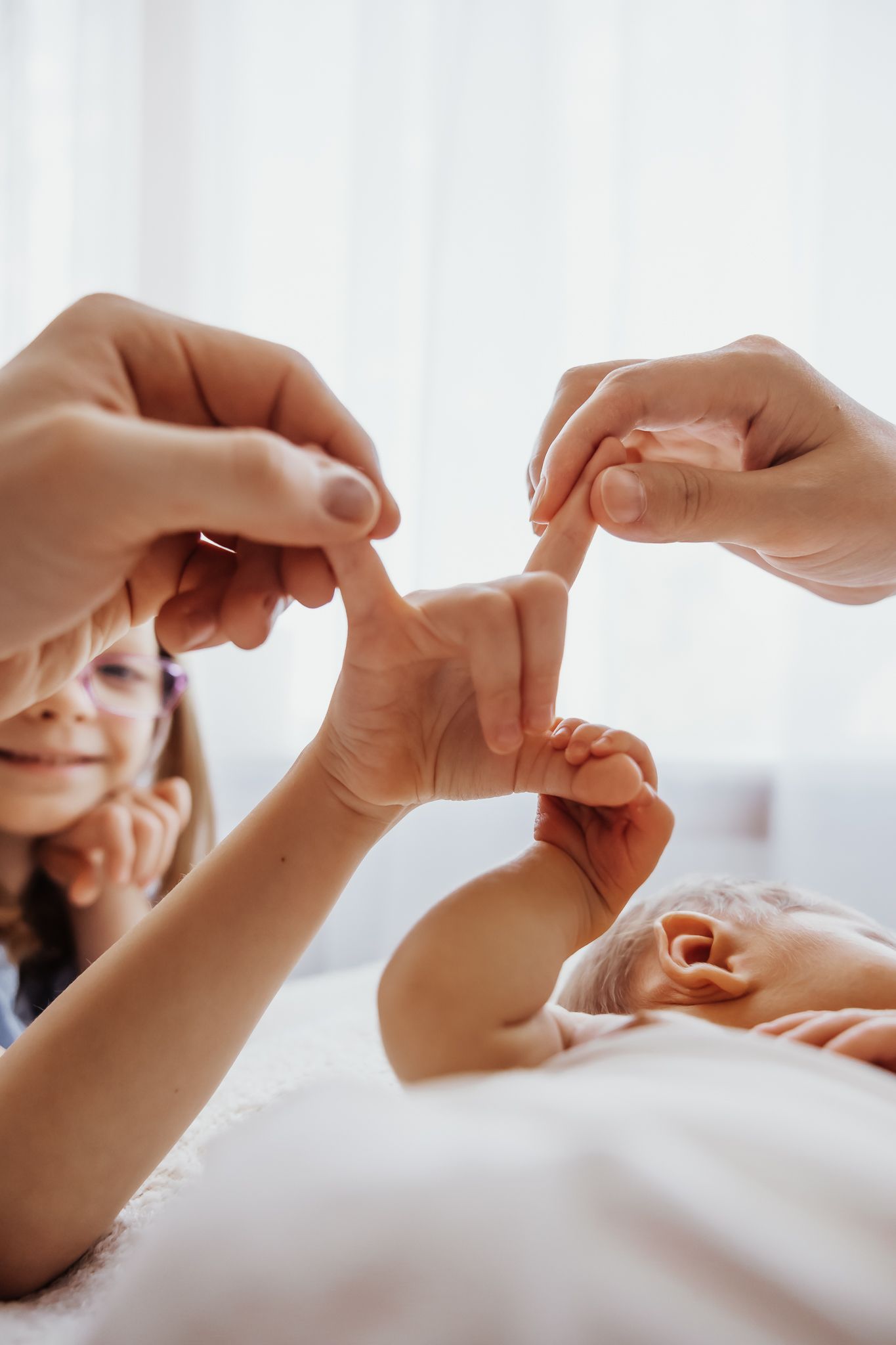 A newborn baby holds fingers of a smiling child and adult in a tender family bonding moment.