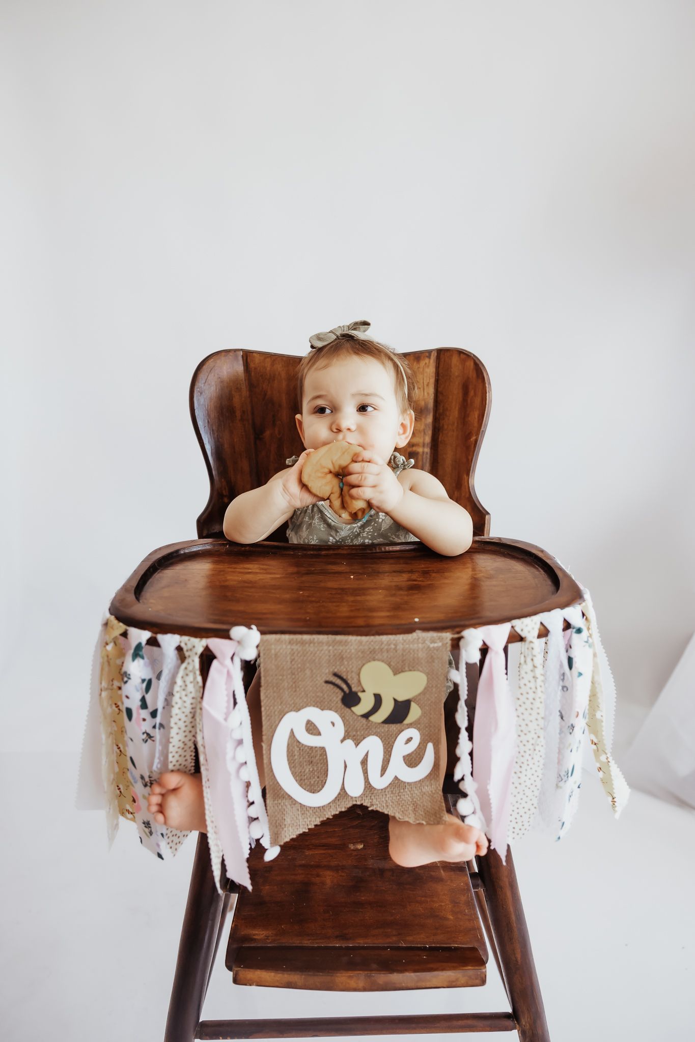 A baby celebrates their first birthday in a wooden high chair, eating cake with a decorative 