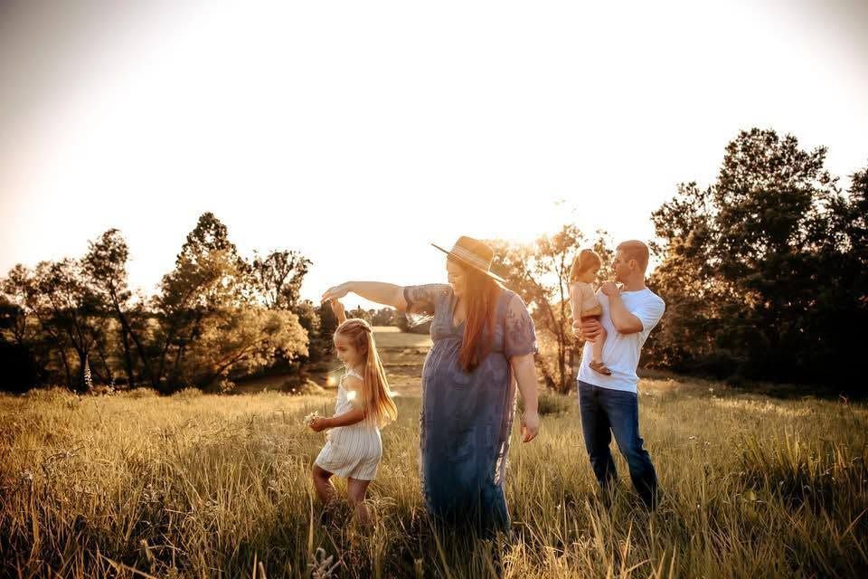 Family enjoying a sunny golden hour meadow session with children and parents in open field.