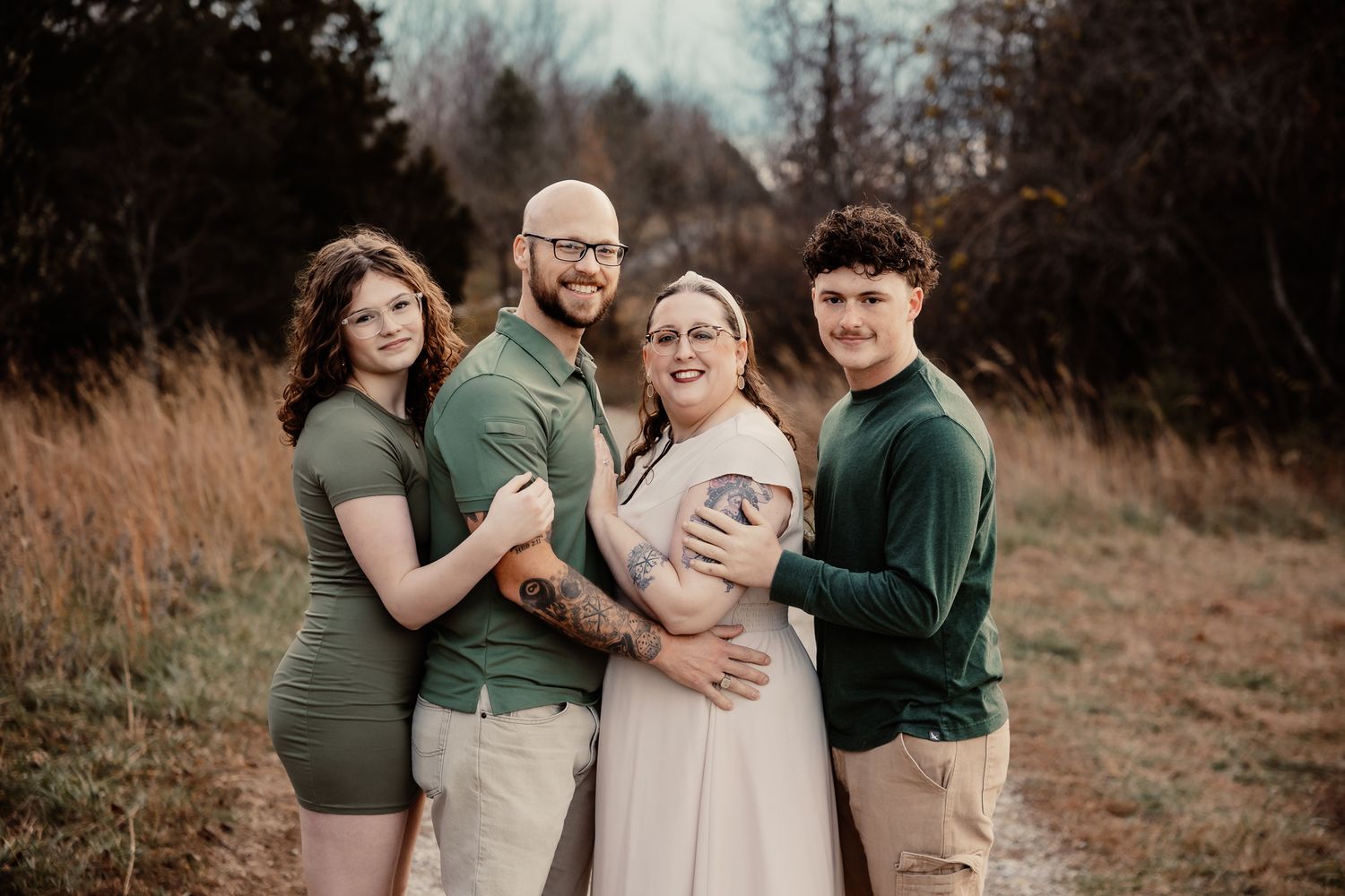 Family of four posing outdoors in coordinating green outfits in a field with tall grass and trees.